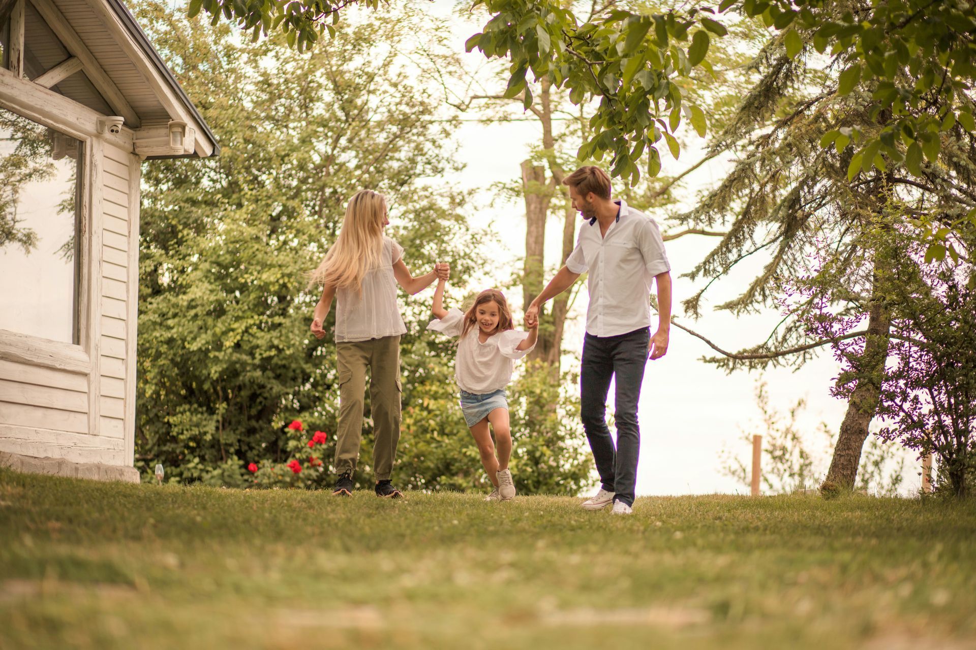 Family of three walking and laughing on a grassy lawn near a white house.