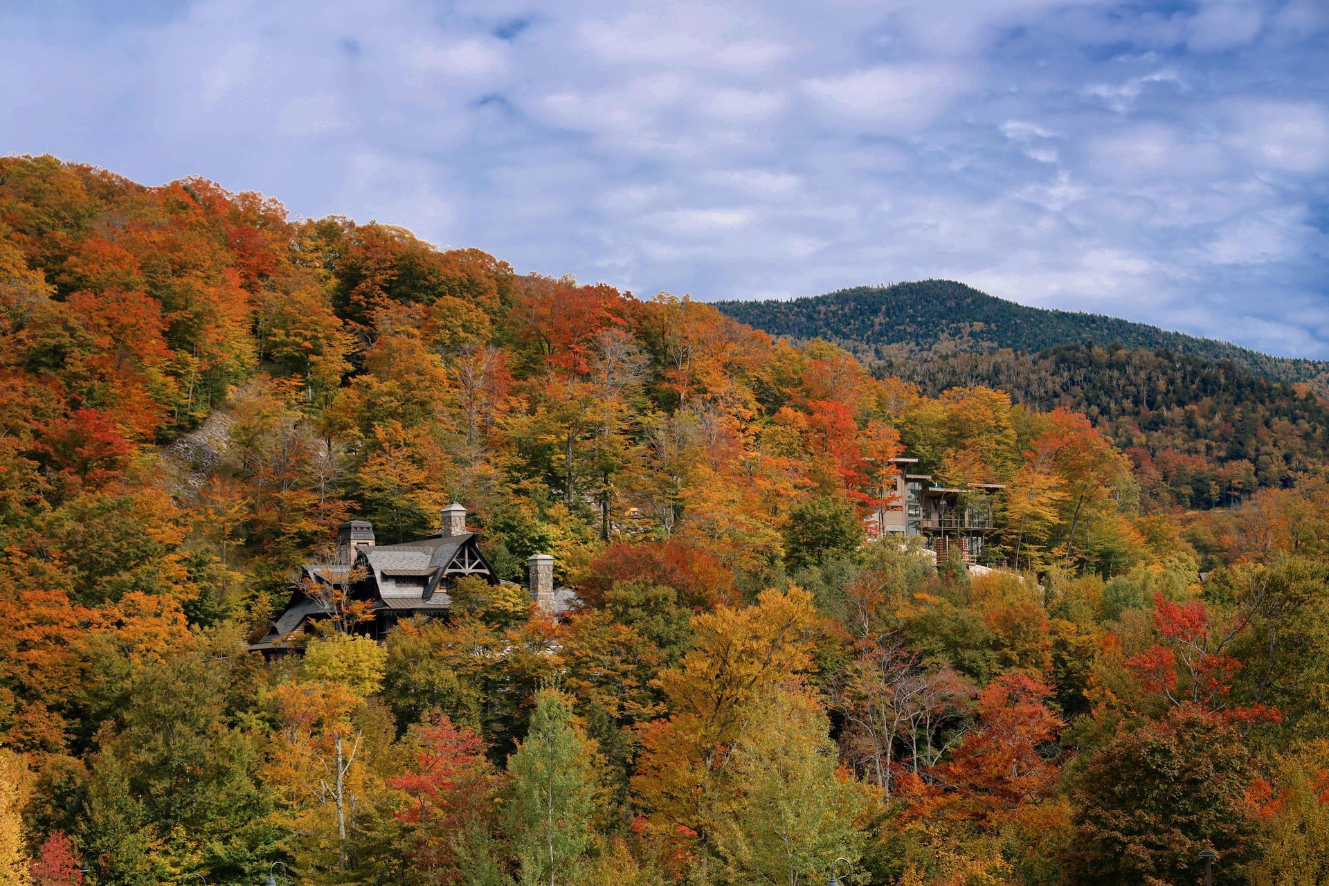 Autumn mountain landscape with houses nestled among trees with vibrant orange, red, and yellow leaves.