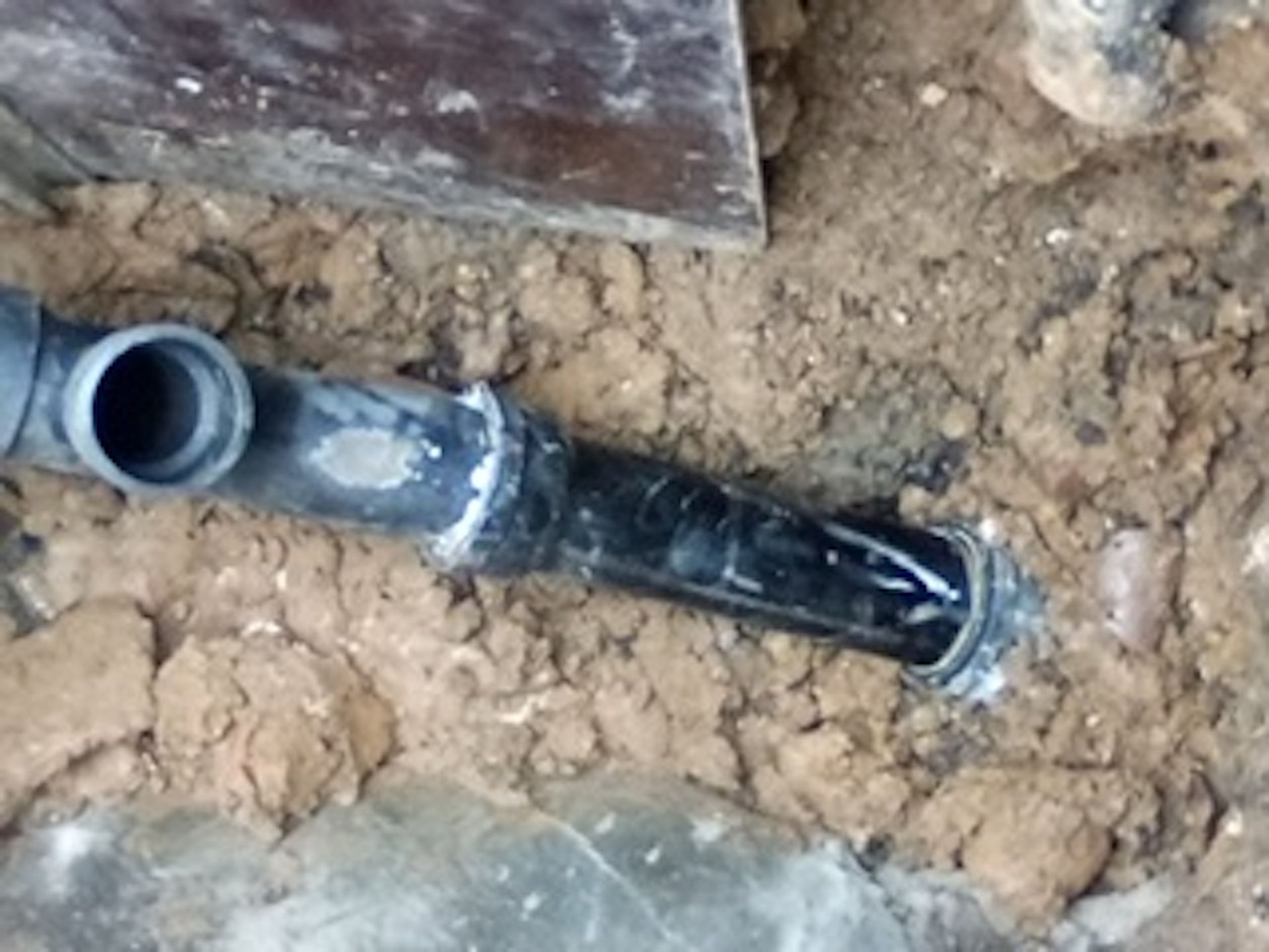 A black pipe is laying in the dirt next to a shovel.