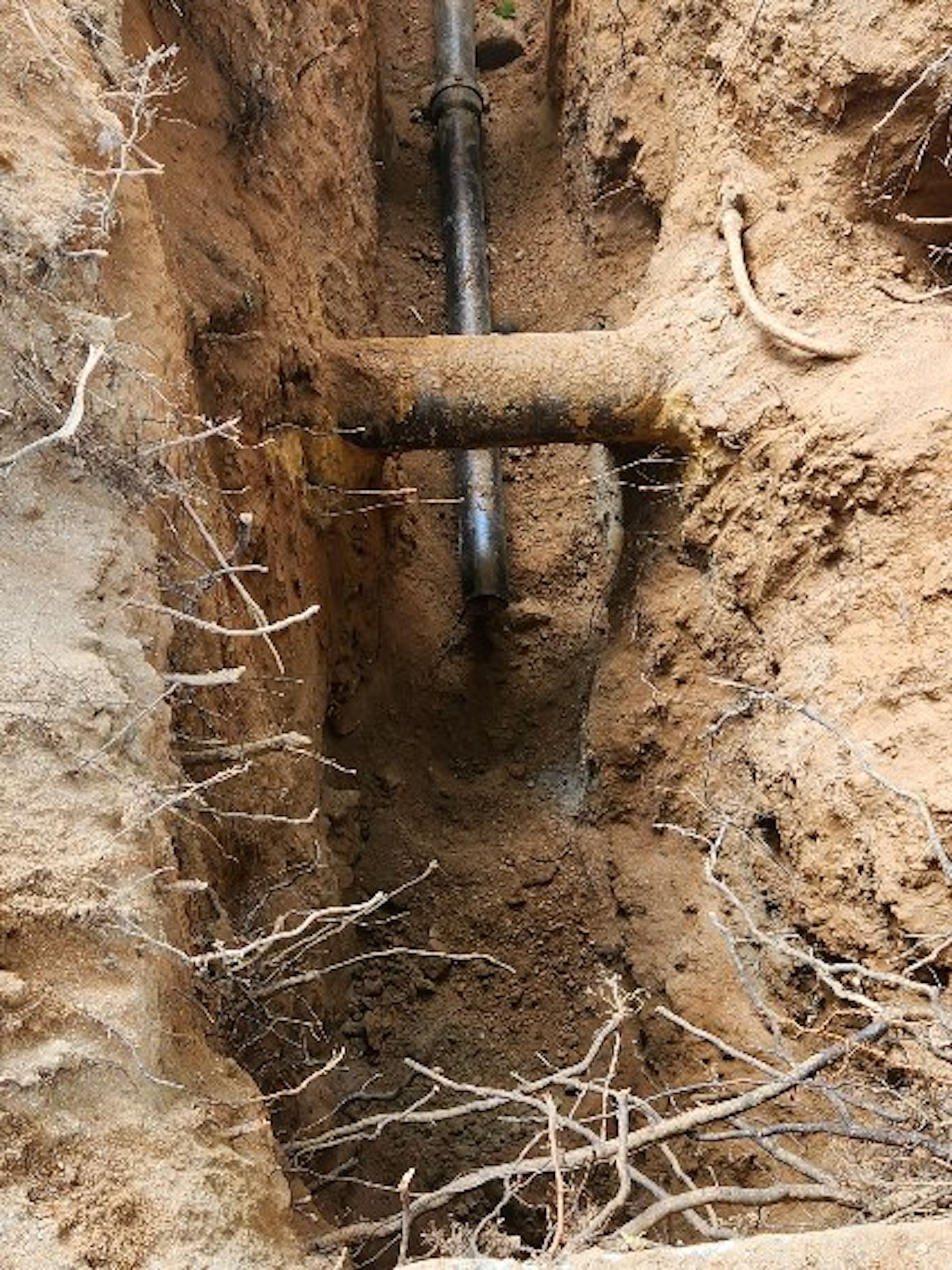 A pipe is laying in the dirt in a trench.