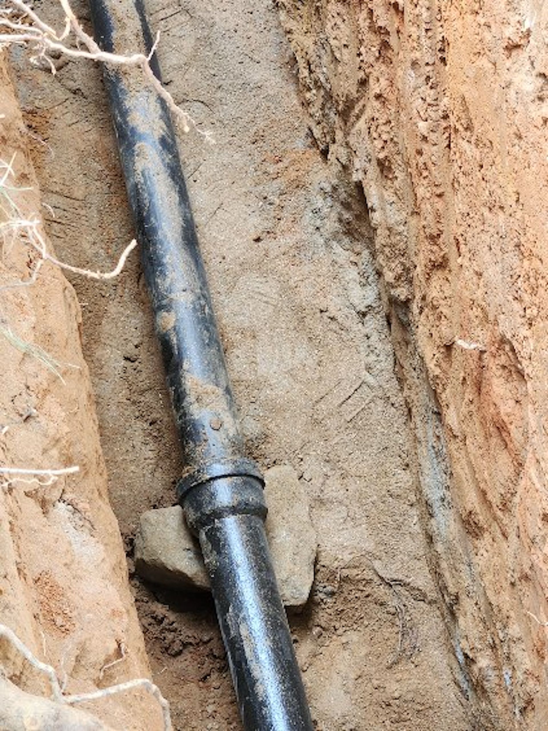 A black pipe is laying in the dirt next to a rock.