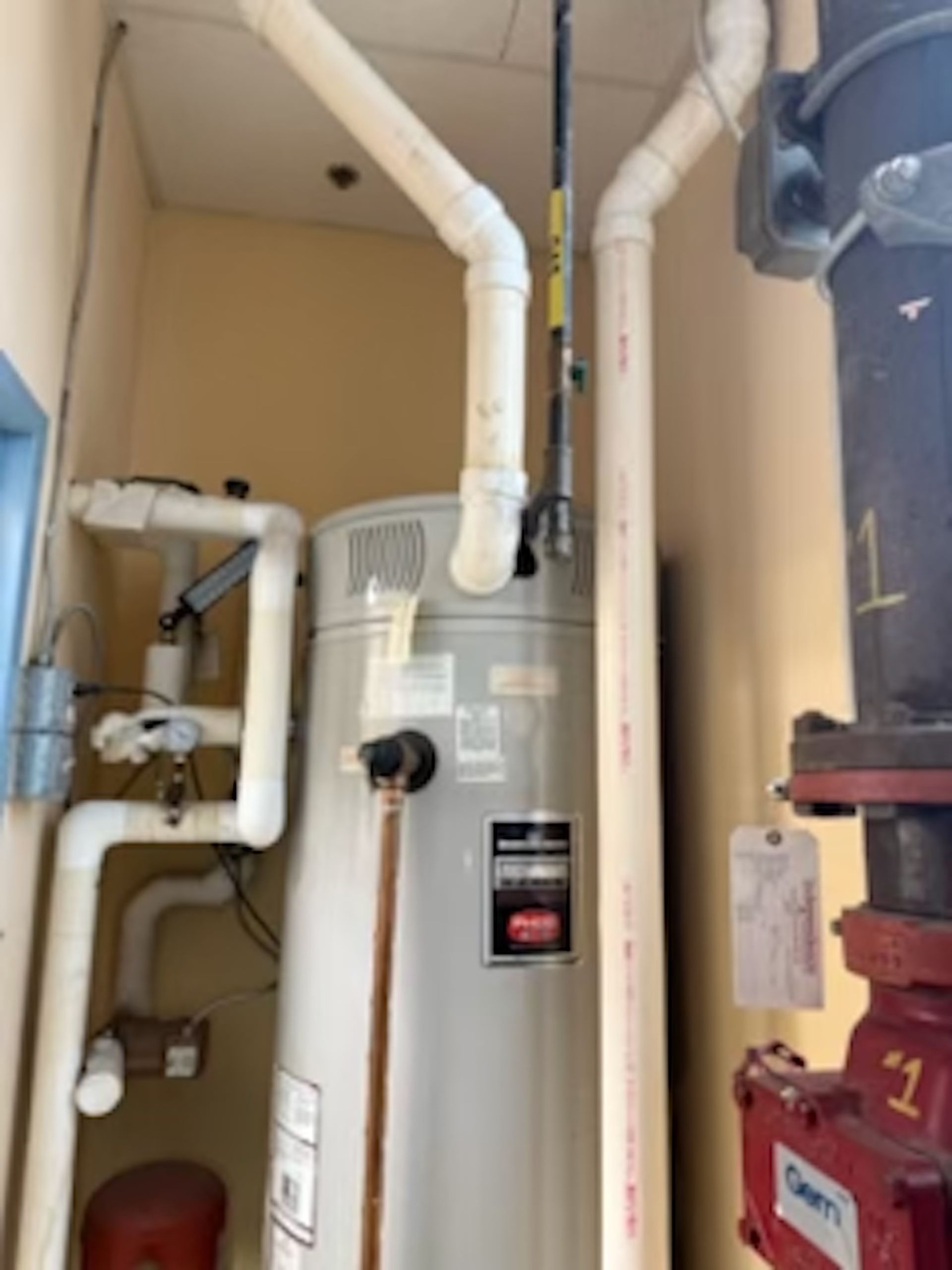 A white water heater is in a room with pipes