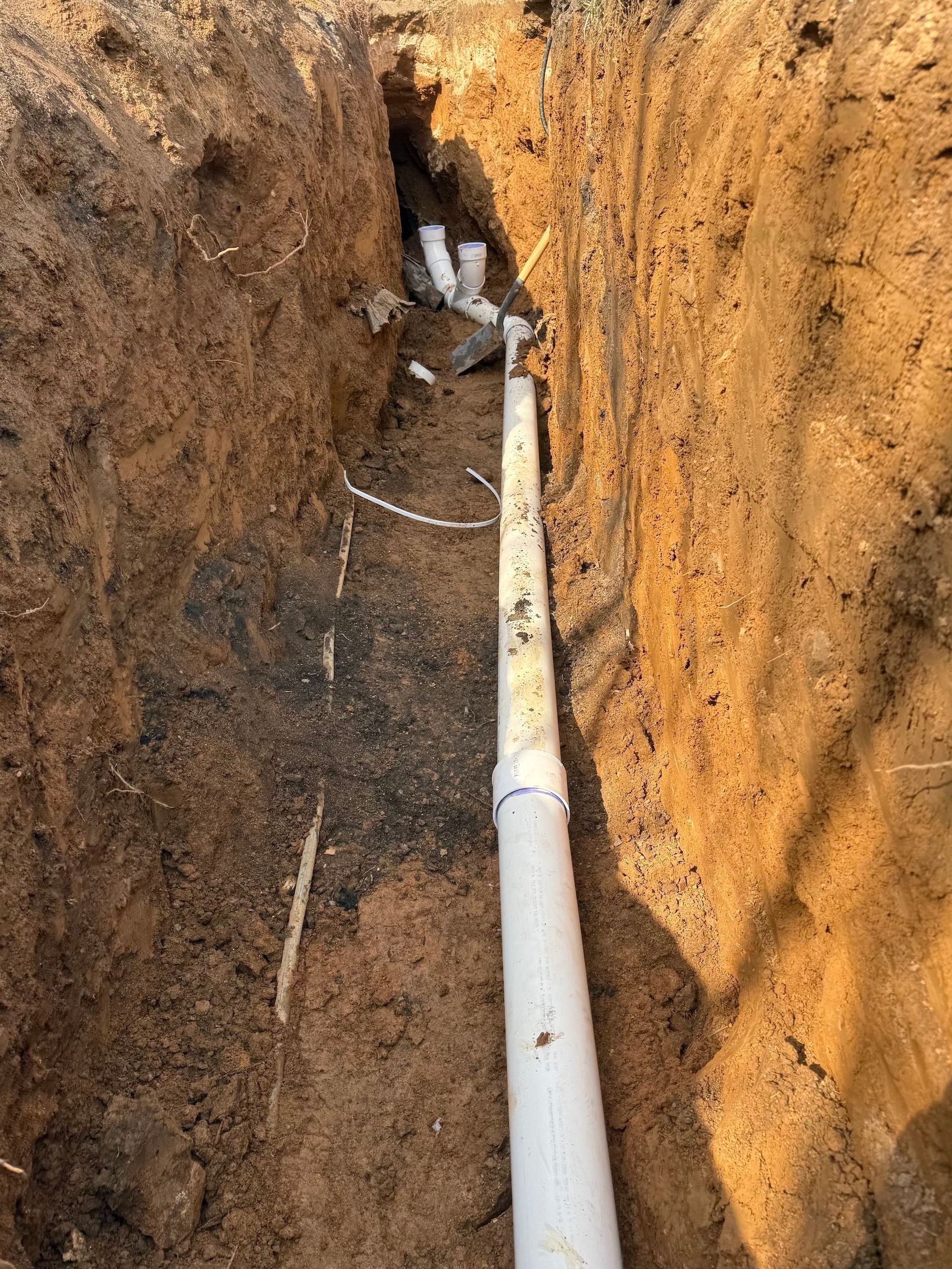 A white pipe is laying in the dirt in a trench.