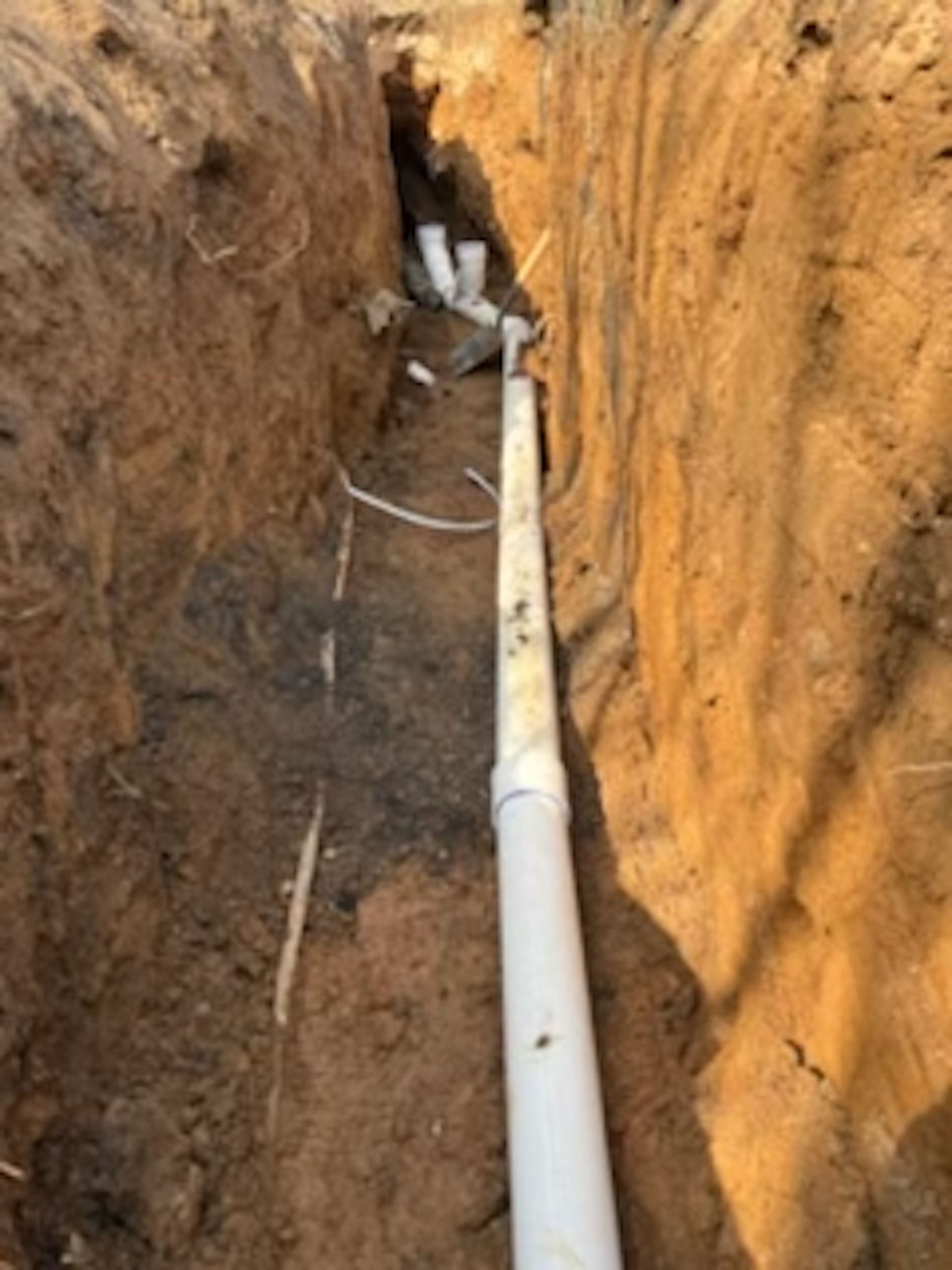 A white pipe is laying in the dirt in a trench.