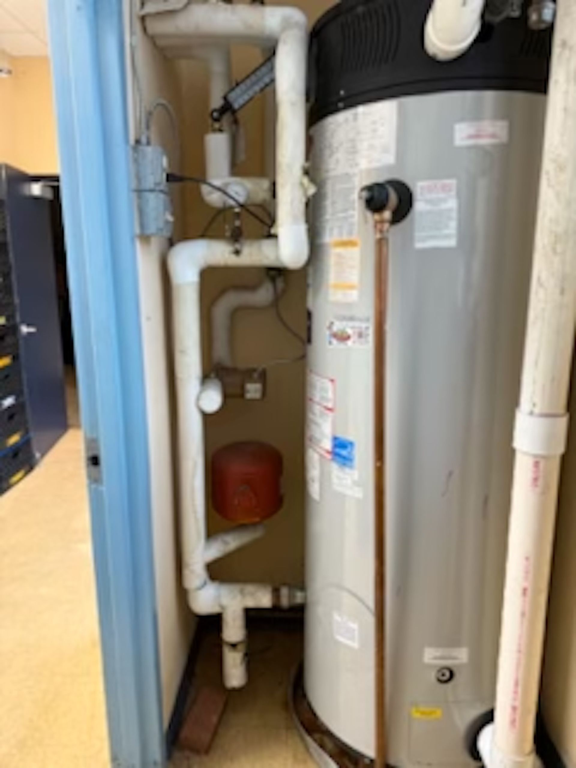 A water heater is sitting in a corner of a room next to a door.