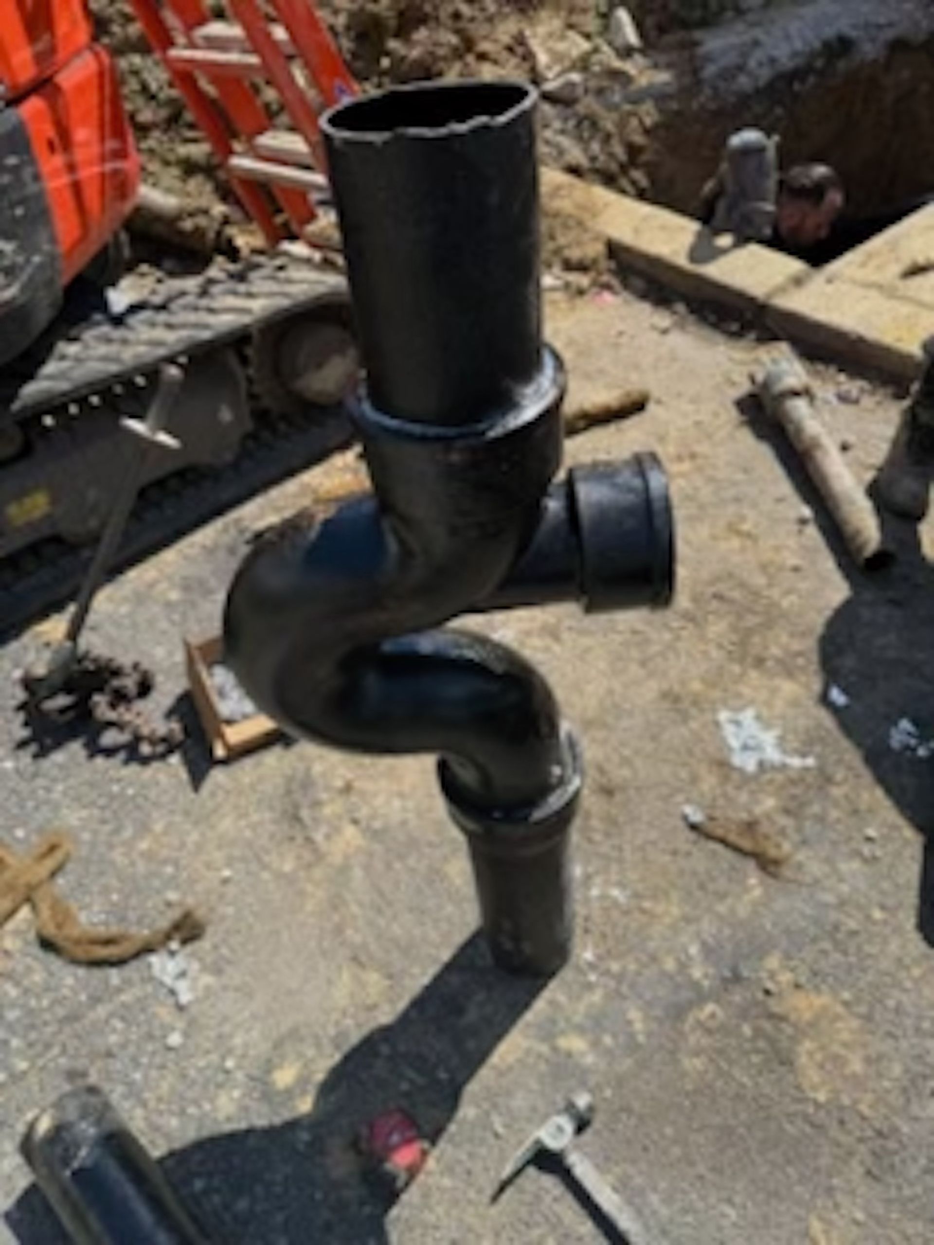 A black pipe is sitting on the ground next to a hammer.