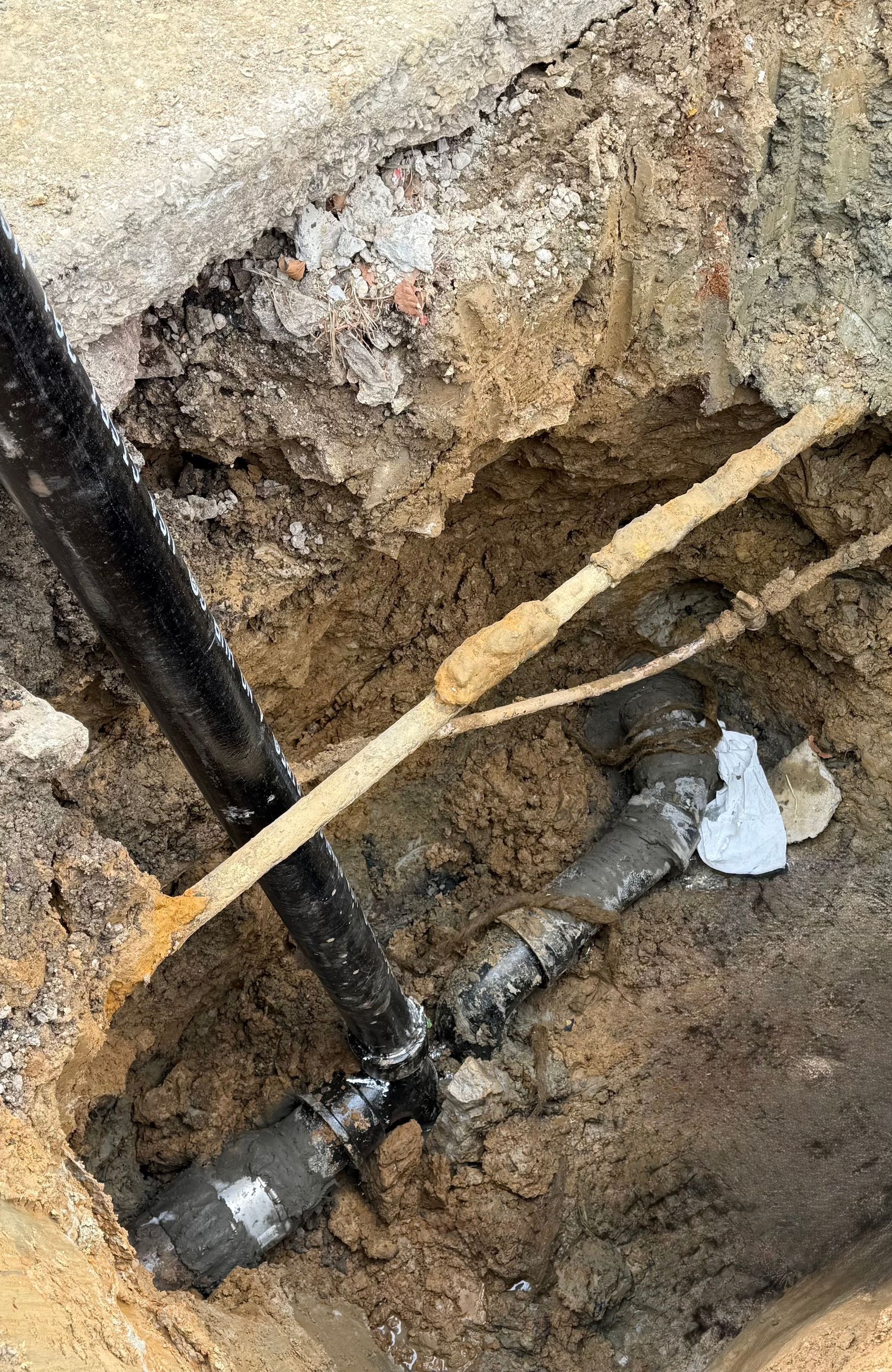 A pipe is laying in the dirt next to a pole.