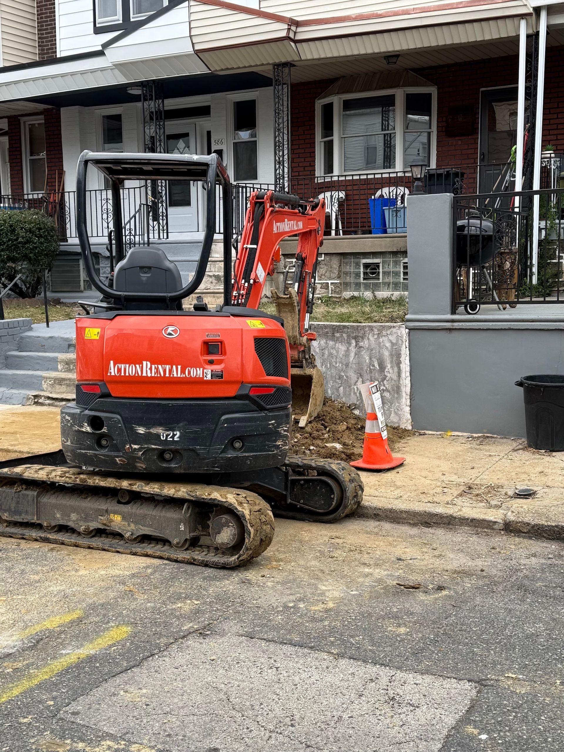 A small excavator is sitting on the side of the road in front of a house.
