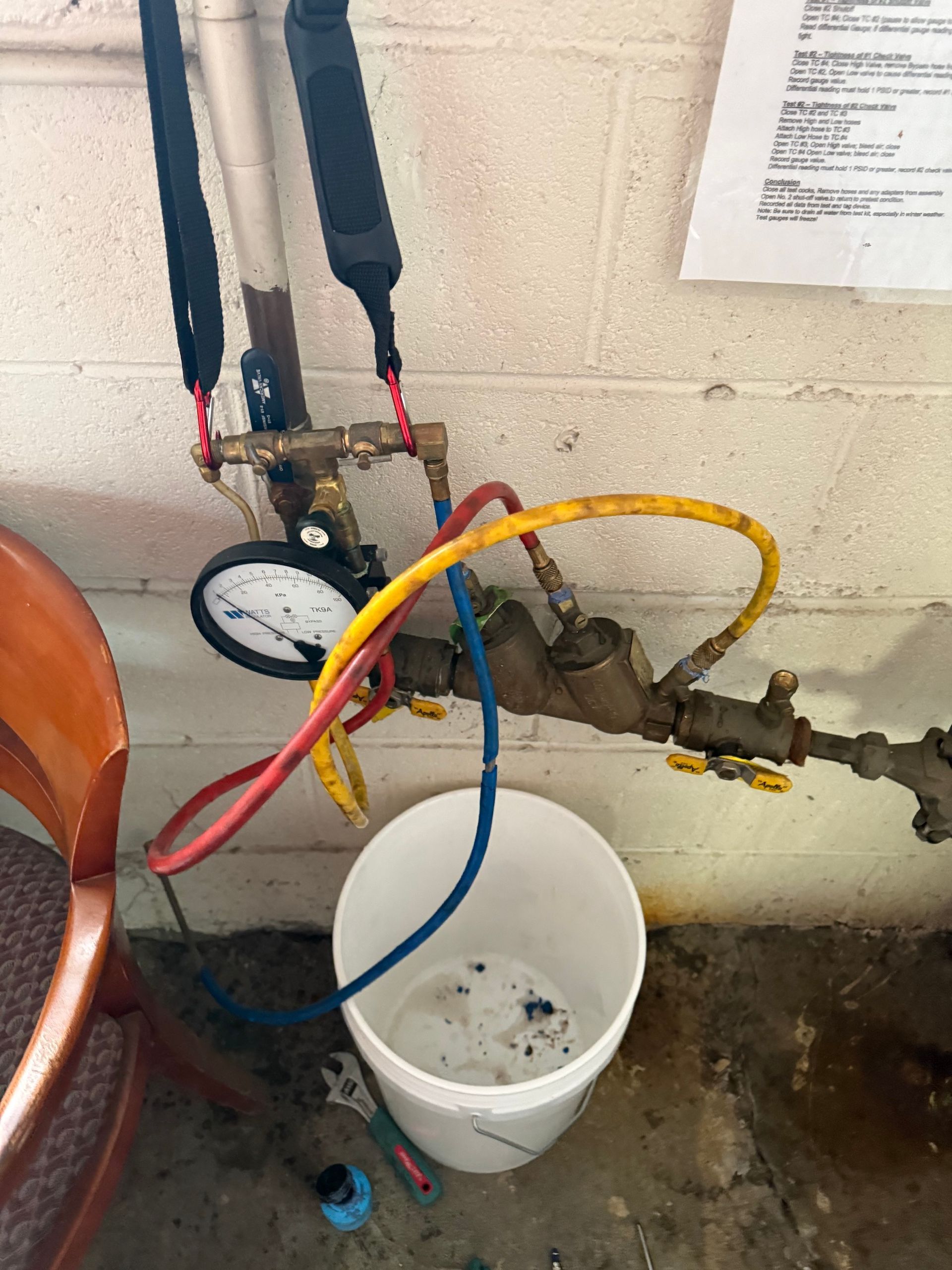 A white bucket is sitting next to a hose with a gauge attached to it