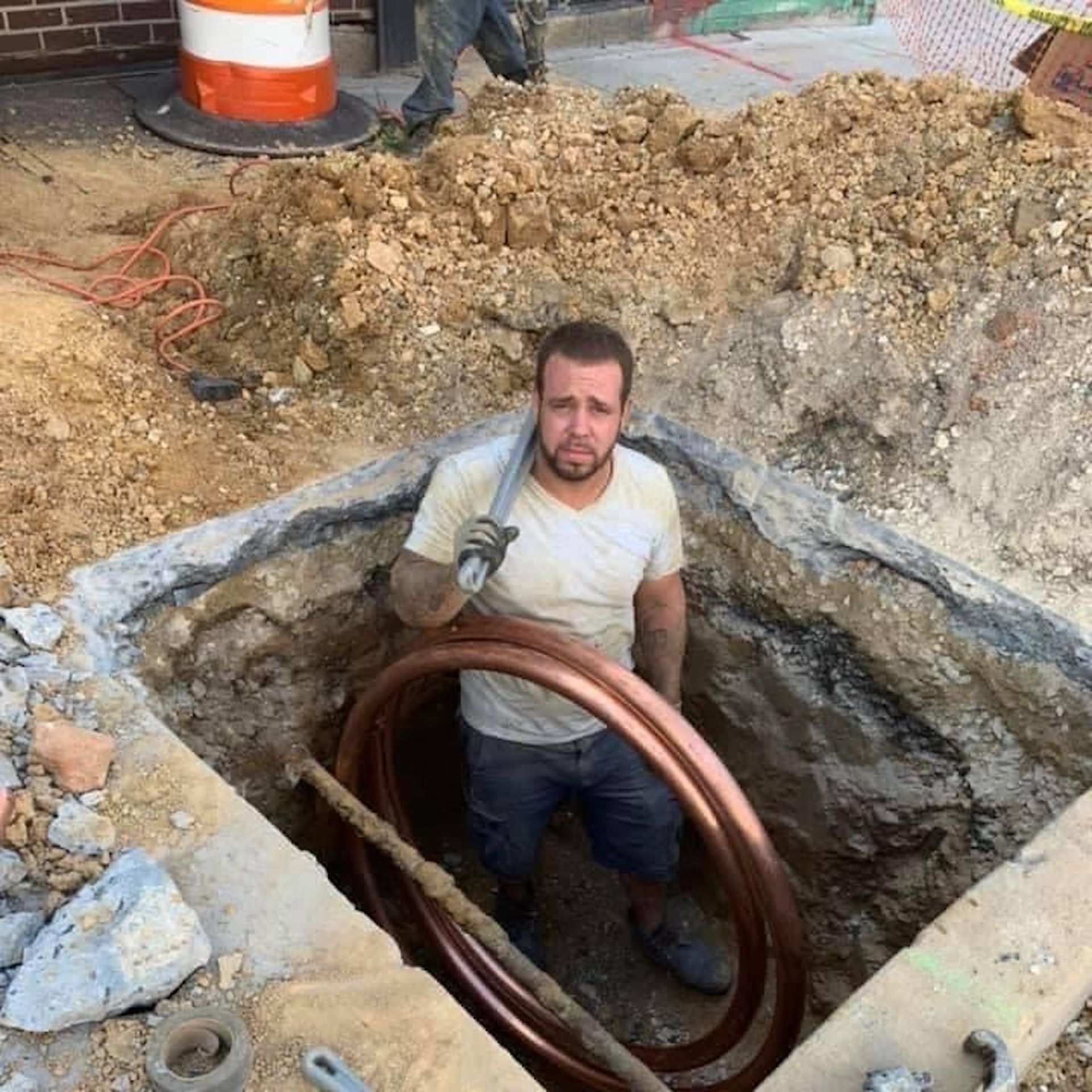 A man is standing in a hole holding a copper pipe.