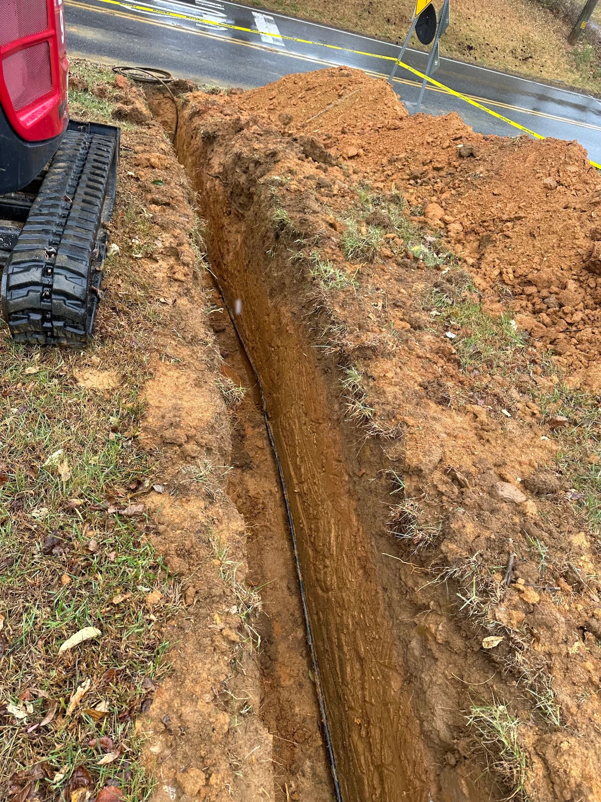 A tractor is digging a trench in the dirt next to a road.