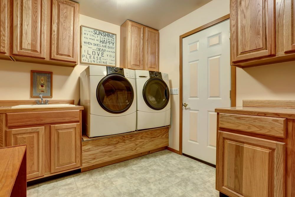 A Laundry Room With A Washer And Dryer And Wooden Cabinets — Standfast Cabinets In Tuggerah, NSW