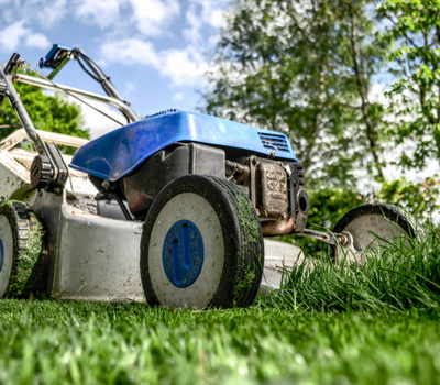 A blue and silver lawnmower cuts through tall green grass under a partly cloudy sky.