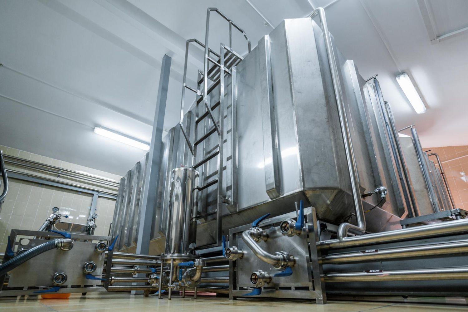 A warehouse filled with lots of stainless steel tanks and pipes.