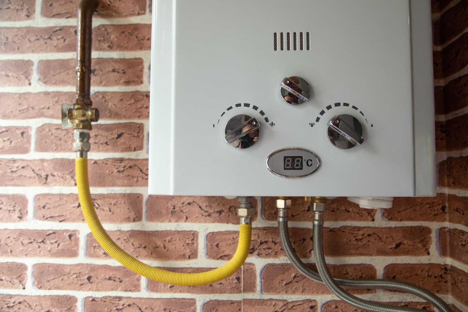 A gas water heater is attached to a brick wall.