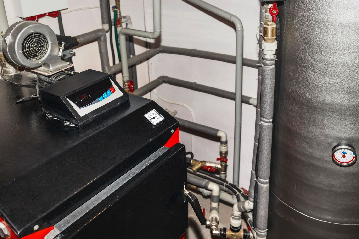 A black and red boiler is sitting in a room with pipes.