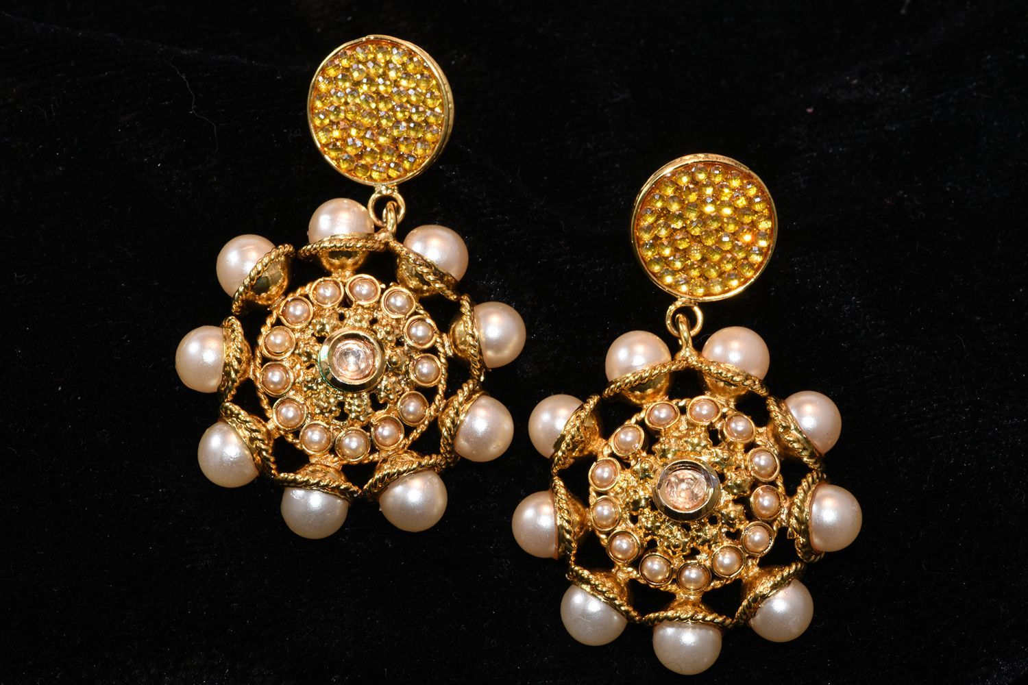 Gold earrings with pearl accents, against a black backdrop.