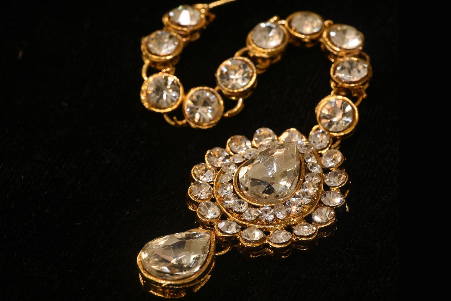 Gold and diamond maang tikka, ornate headpiece with a large central gem, on a black surface. Gold and diamond maang tikka, ornate headpiece with a large central gem, on a black surface.