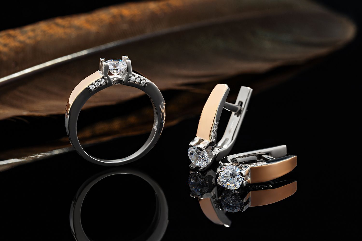 Ring and earrings with diamonds and gold accents on a black surface with a feather. Ring and earrings with diamonds and gold accents on a black surface with a feather.