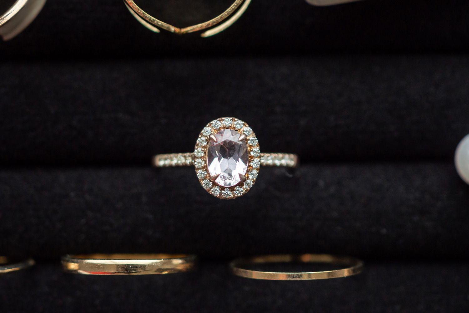 Oval-cut peach gemstone ring with diamond halo on black velvet jewelry display.