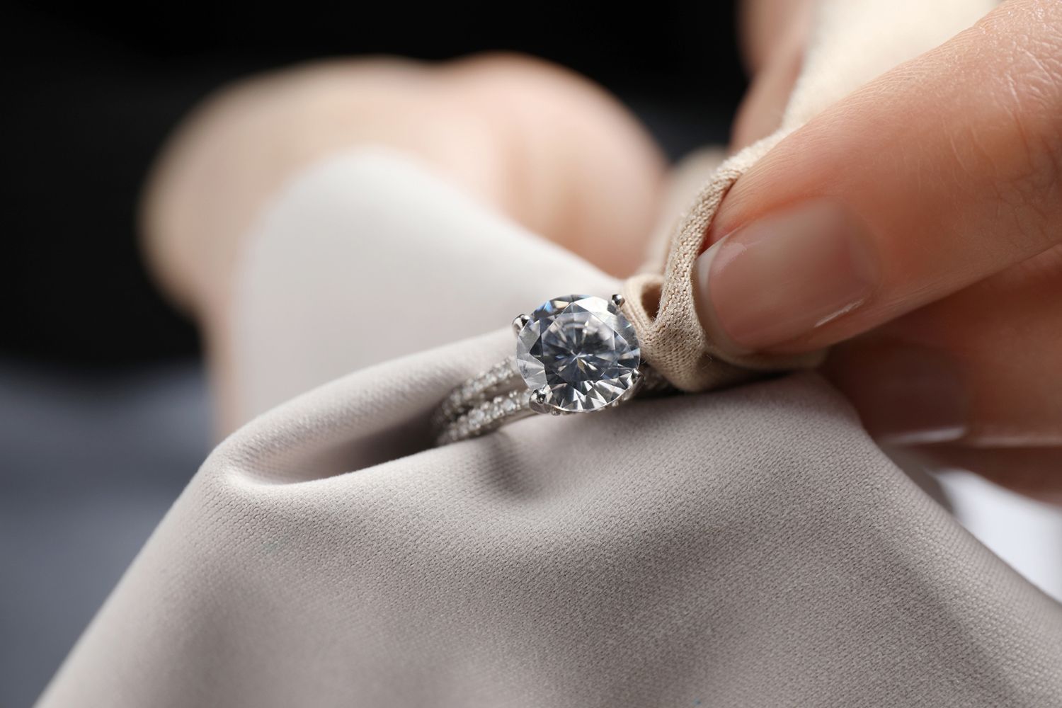Hand polishing a diamond ring with a soft, beige cloth.