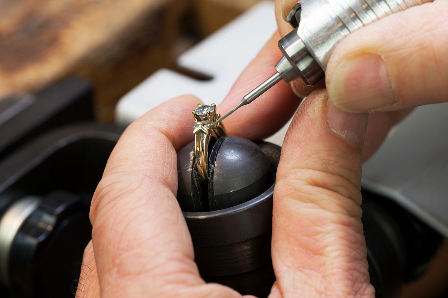 Jeweler using a rotary tool to work on a ring held in a clamp.