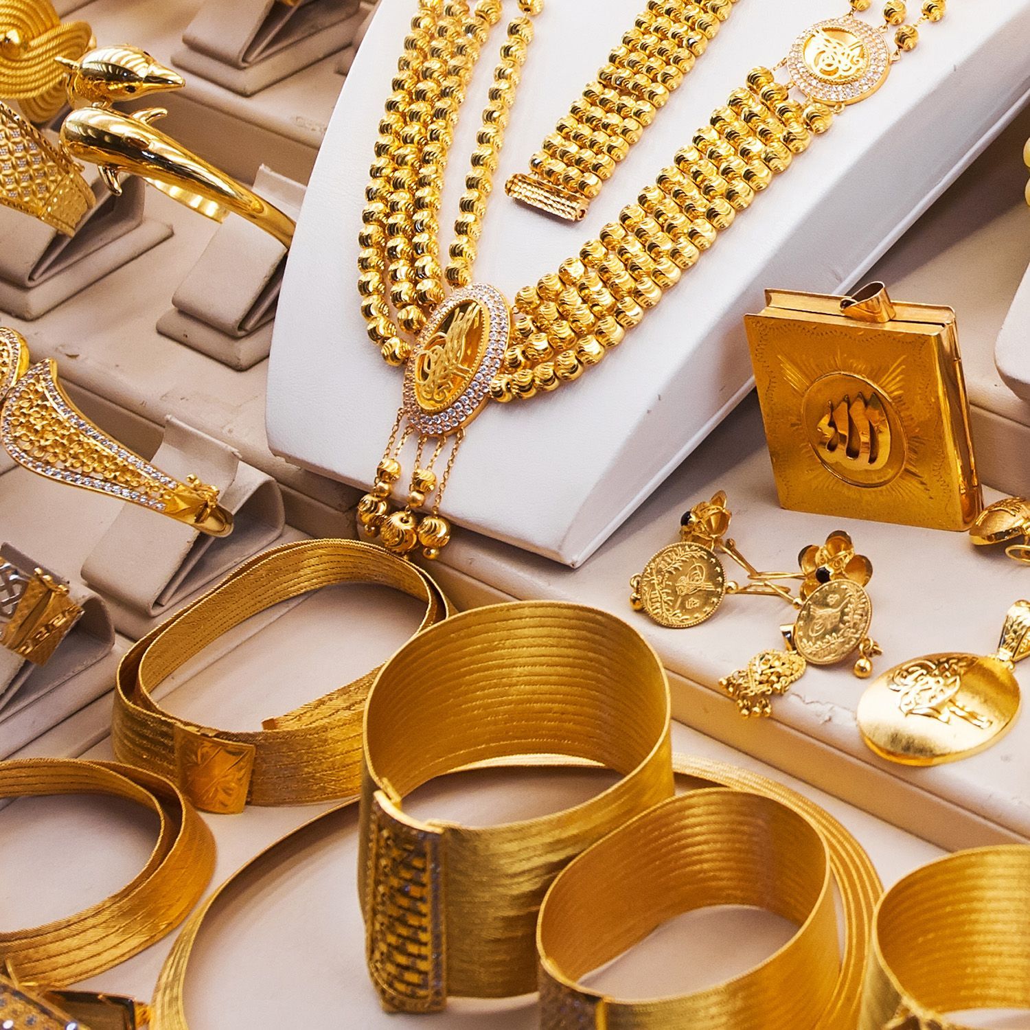 Gold jewelry display: necklaces, bracelets, earrings, and rings, brightly lit on white stands.