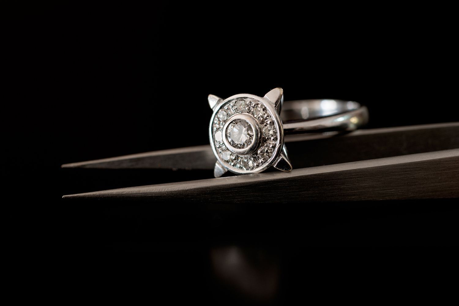 Diamond ring held by tweezers against a black background.