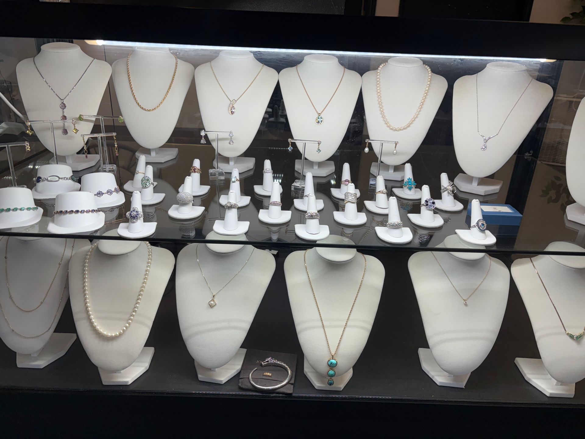 Person's hands holding a gold necklace displayed on a mannequin in a jewelry store.