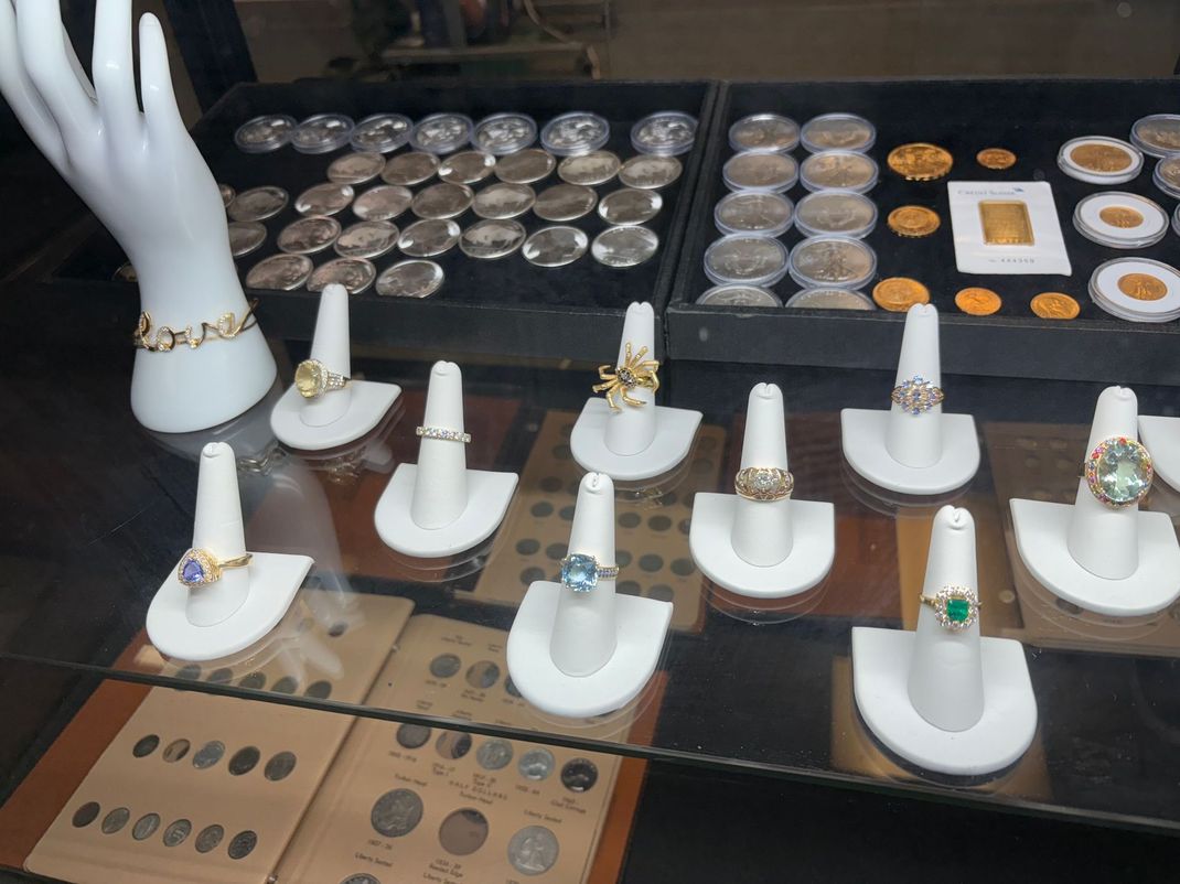 Jewelry display with rings, bracelets, coins, and gold bar in a shop setting.
