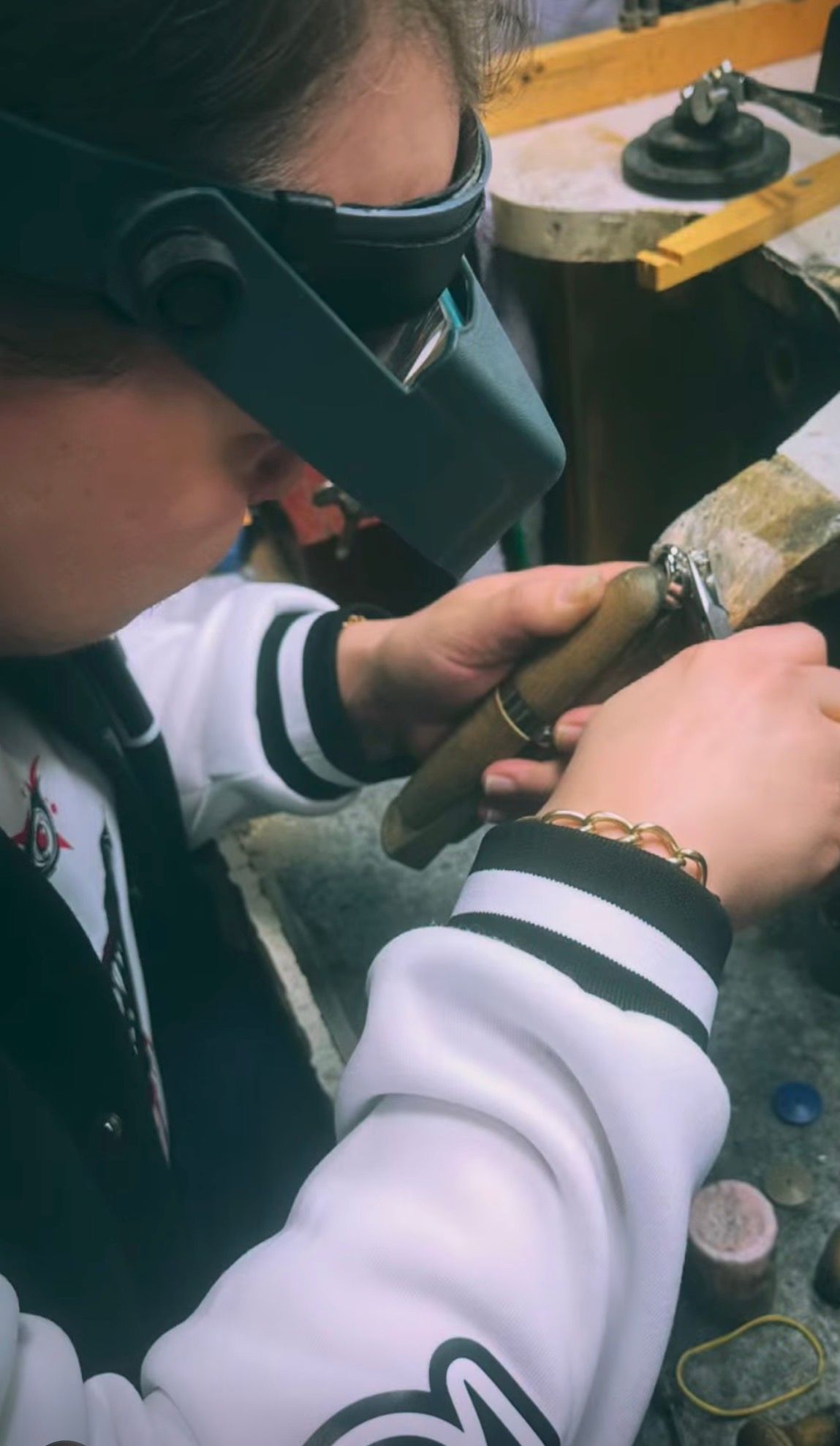 Person wearing a magnifying visor working with small tools on a piece of jewelry.