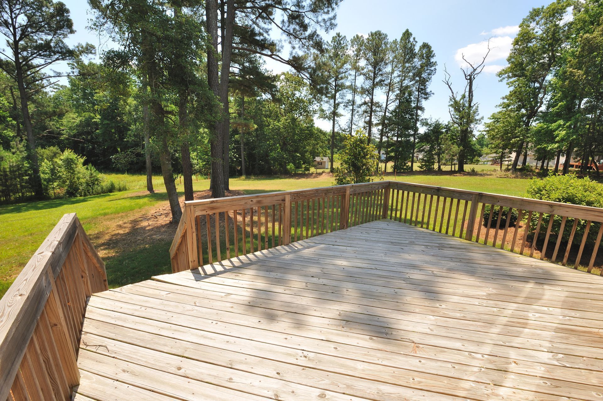 Wooden deck overlooking a sunny green yard with tall trees and a wind turbine in the distance