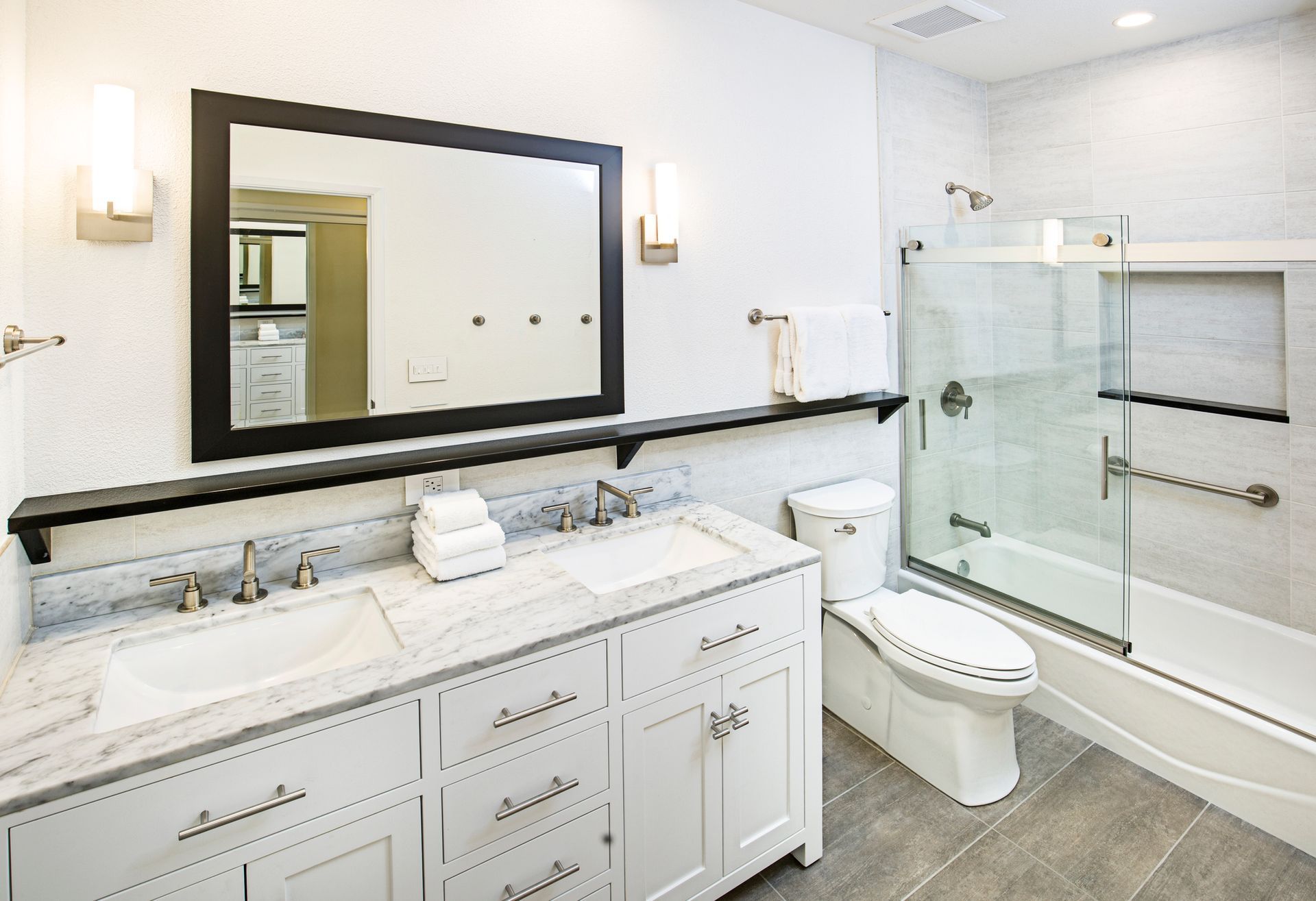 Modern white bathroom with double vanity, large mirror, toilet, and glass-enclosed shower.