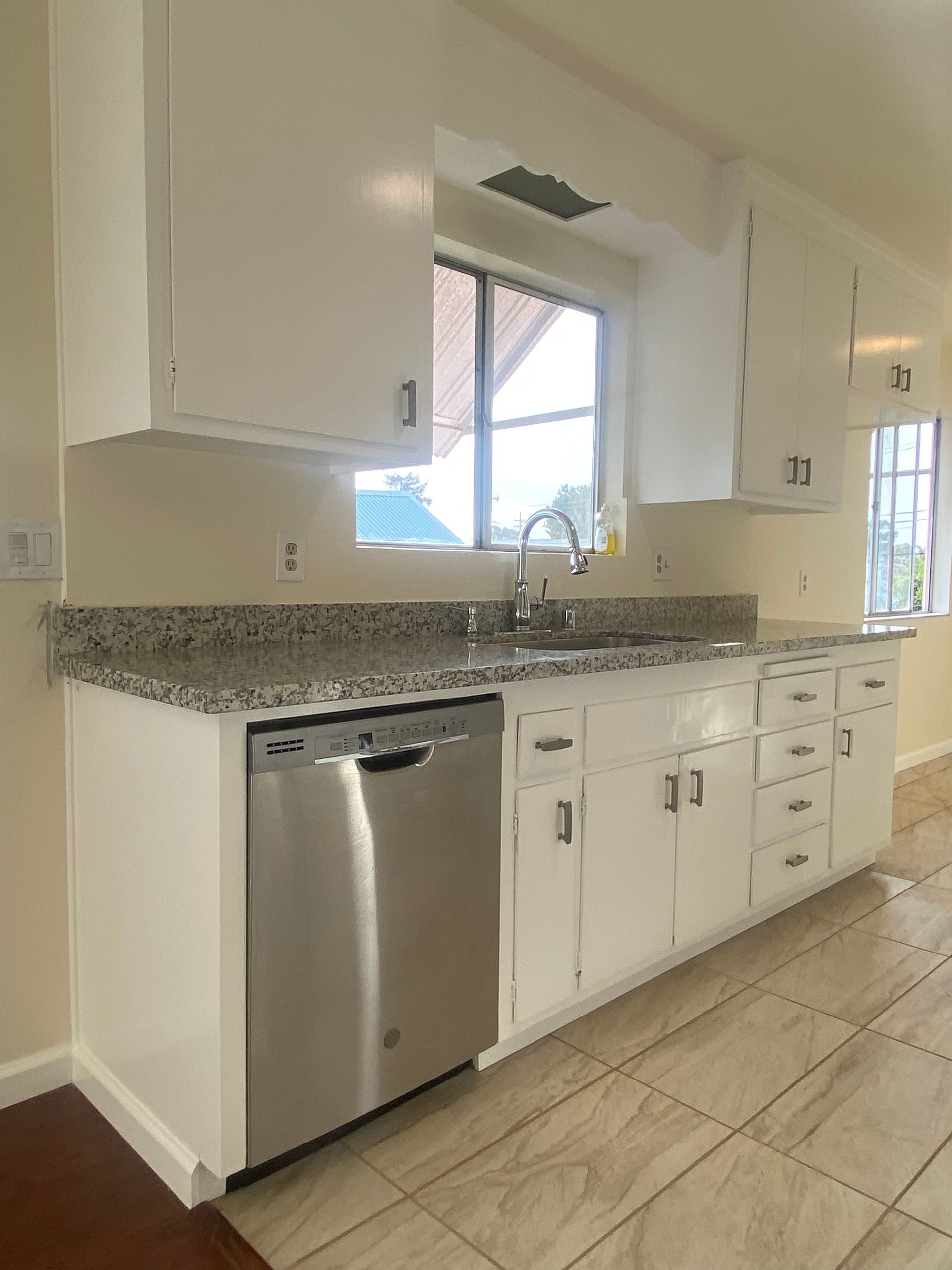 Modern kitchen with white cabinets, stainless dishwasher, granite countertop, and tiled floor