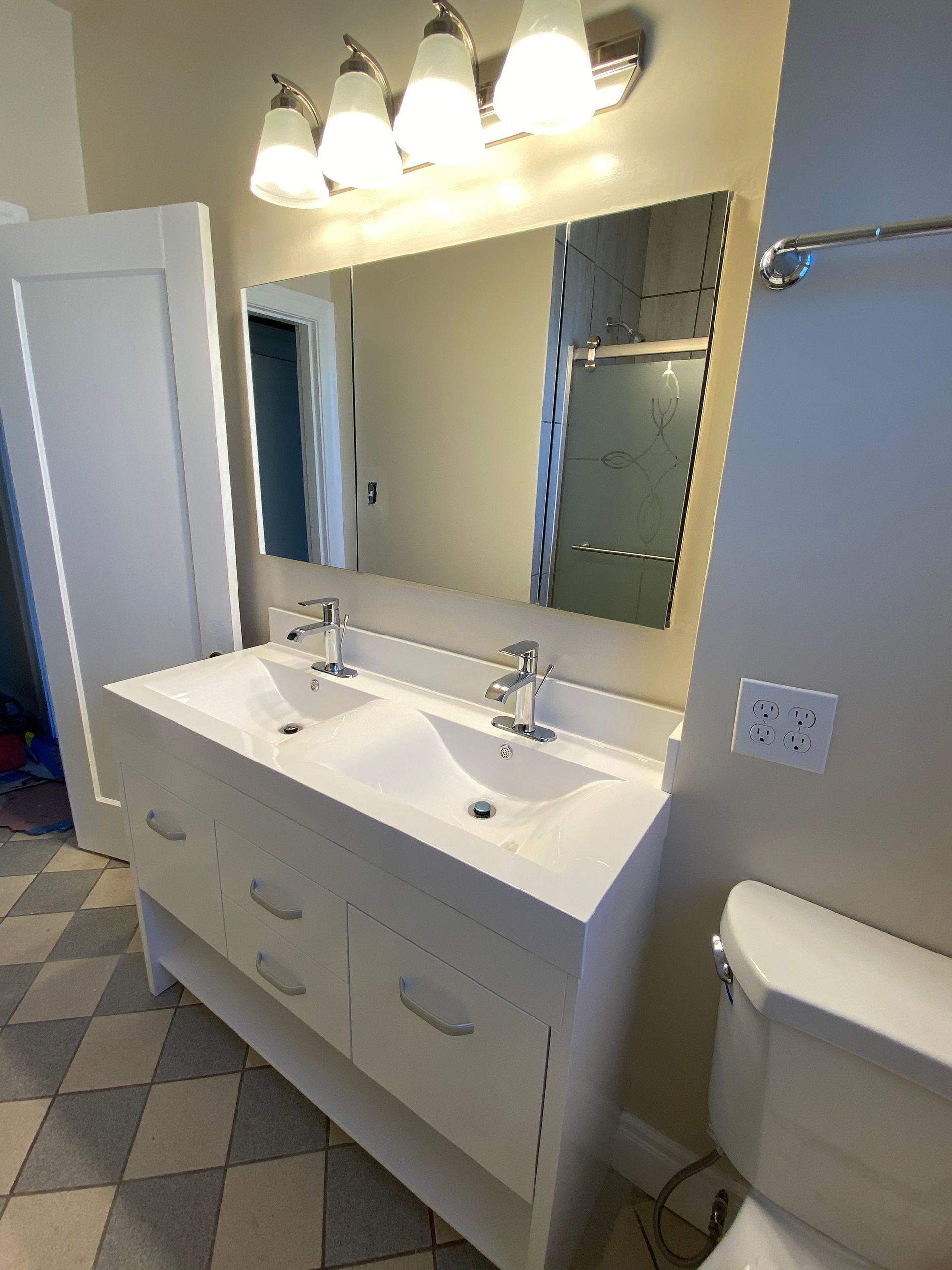 Bathroom vanity with double sinks, large mirror, and wall lights above a toilet.