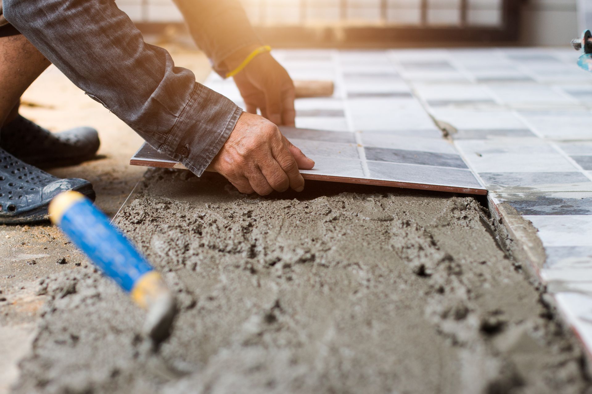 Hands leveling wet concrete beside blue-handled tools on a construction site