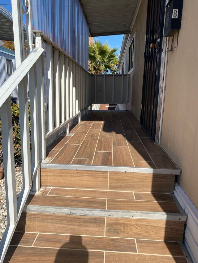 Narrow wooden side walkway with steps between buildings, blue metal railing, and sunlight at the far end