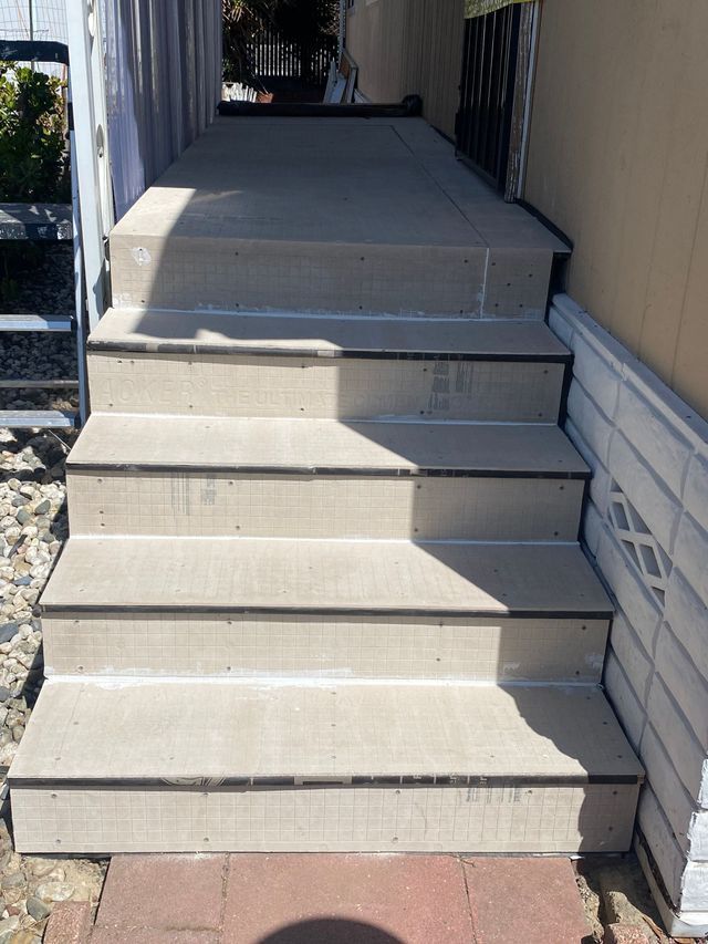 Front steps leading to a porch, with light beige concrete stairs and white siding on both sides.
