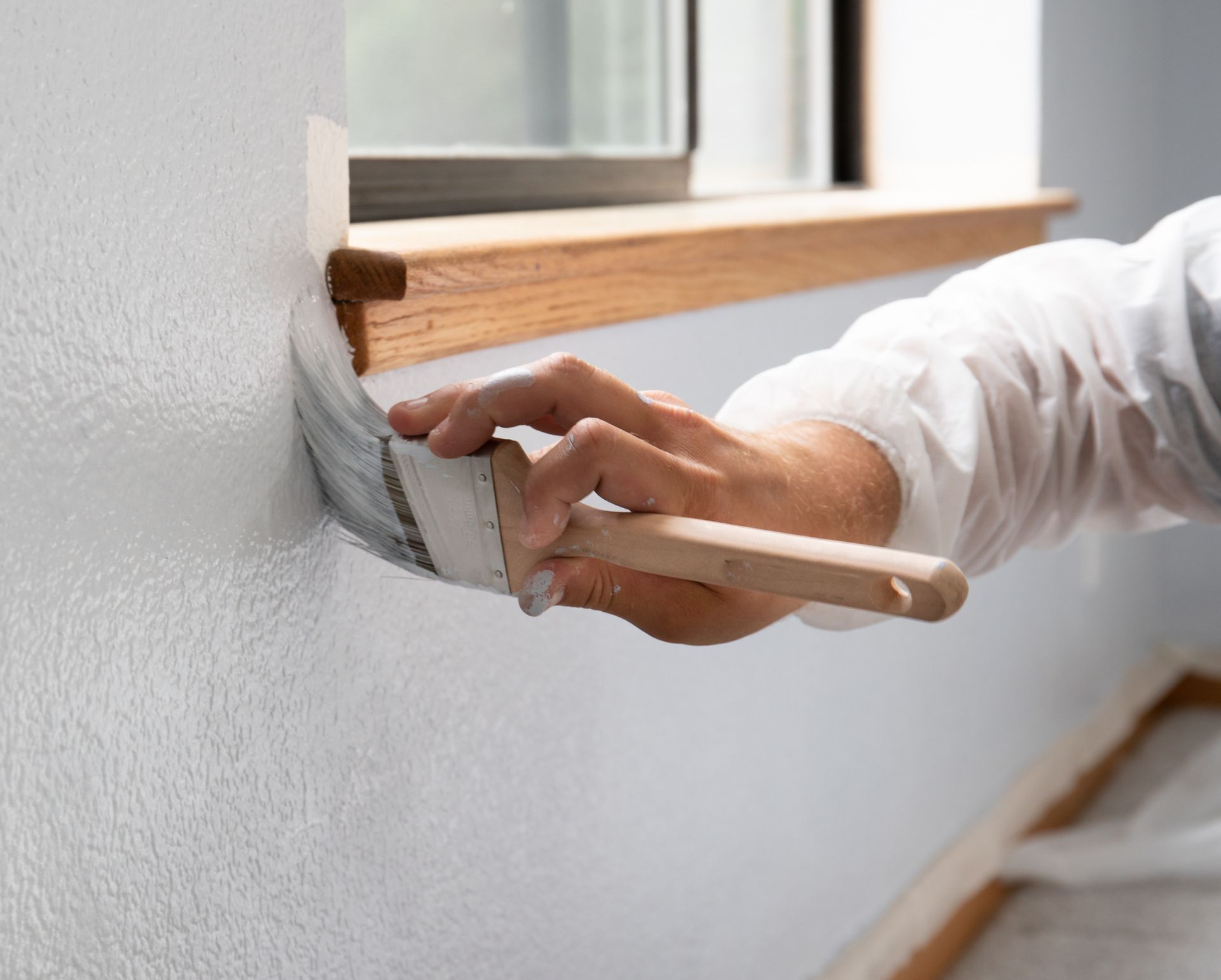 Hand painting white interior wall near a window with a paintbrush