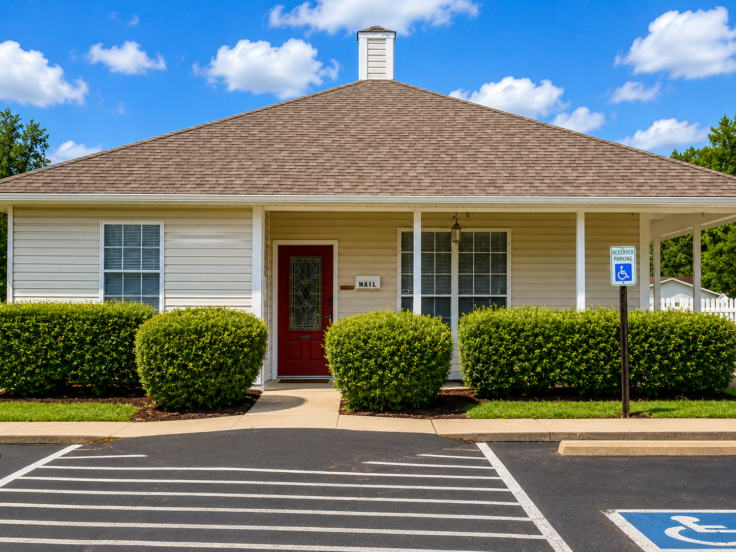 Single-story building with red door, white siding, bushes, and accessible parking space in front.