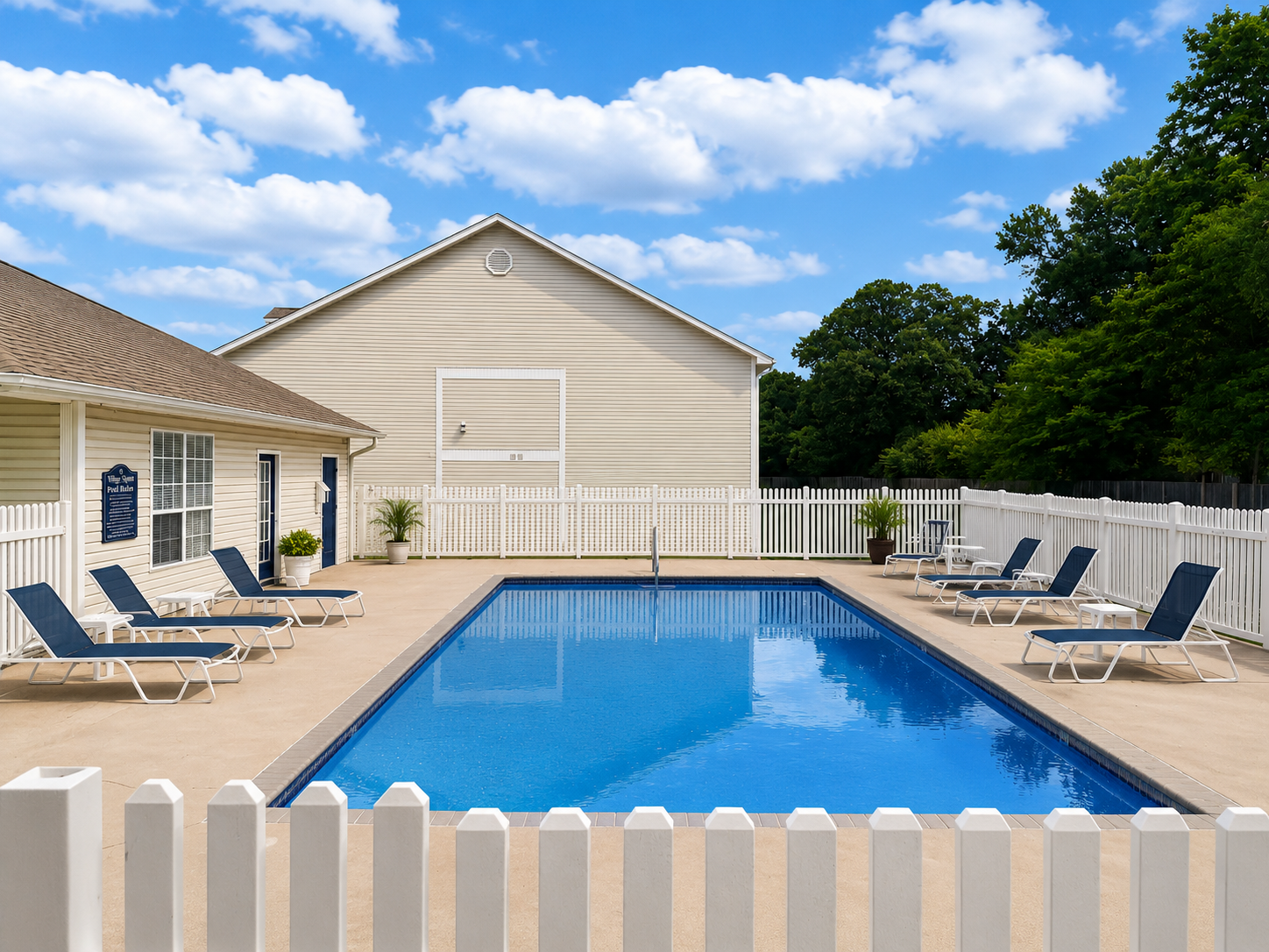 Backyard swimming pool with lounge chairs, white fence, and blue sky with clouds