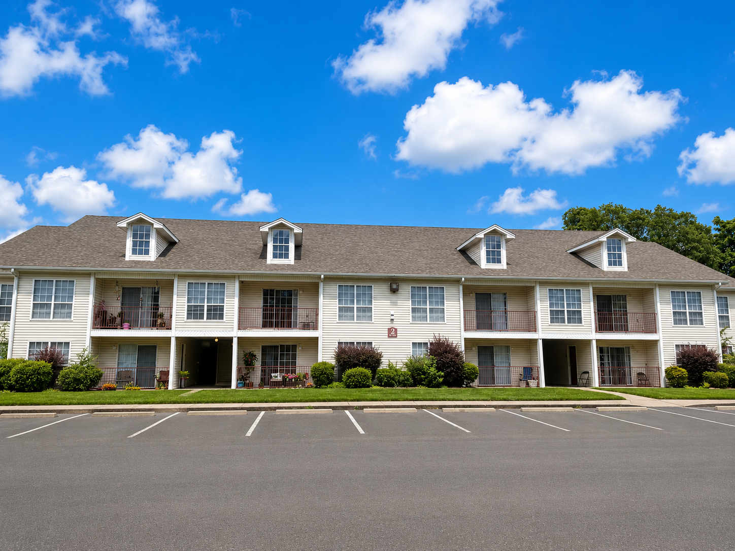 Two-story motel with white balconies and dormer windows under a blue sky, beside an empty parking lot
