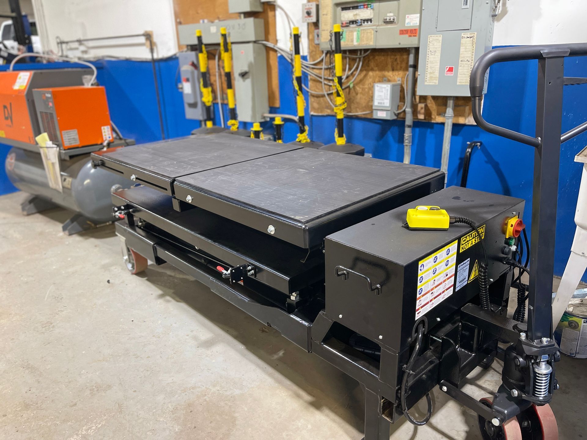 A hydraulic lift table is being pushed by a hand truck.