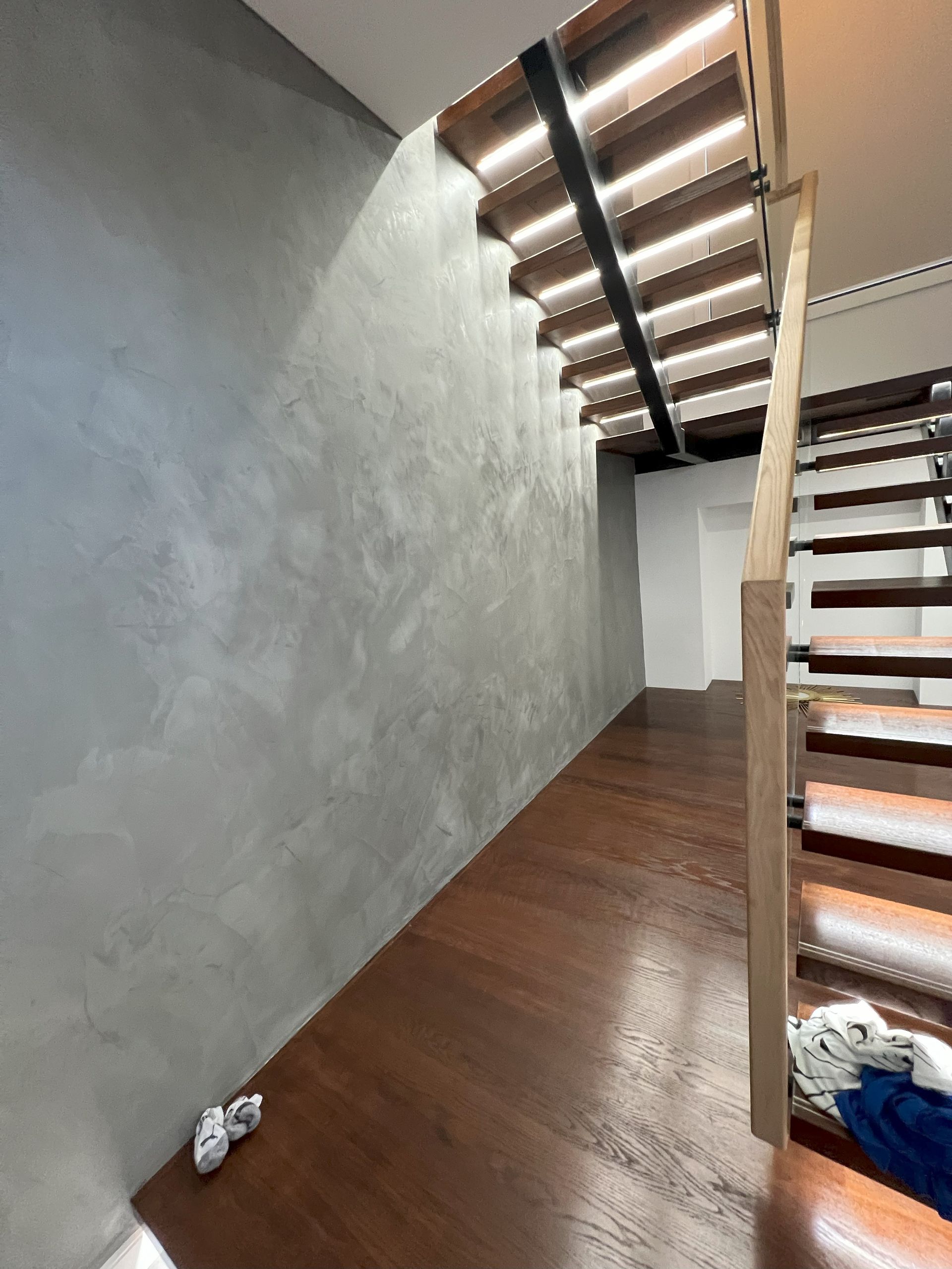 Wooden staircase with natural light, leading to a dark hallway. Gray wall on the left.