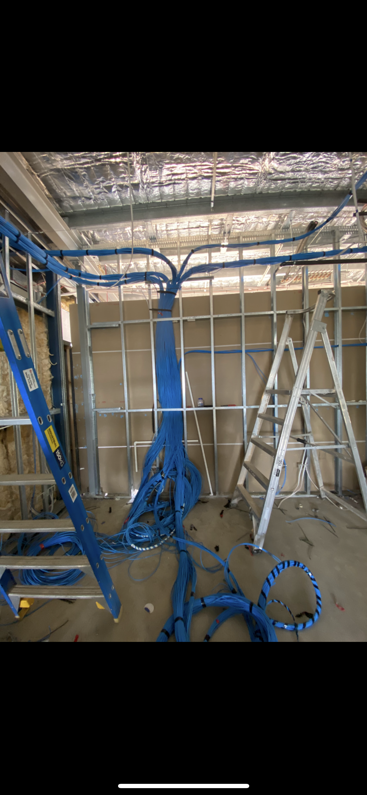 Blue electrical wiring installed on a construction site, with ladders and metal studs visible.