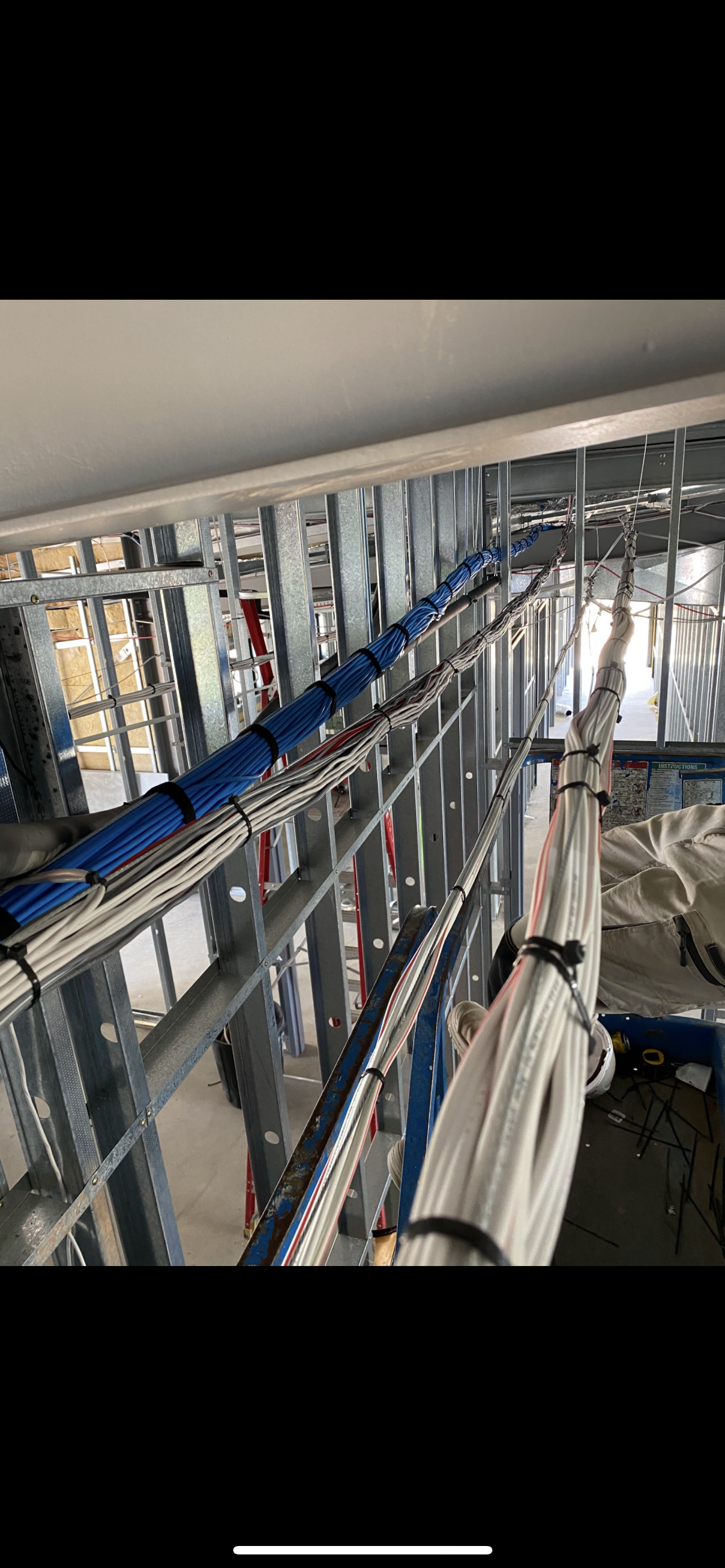 Cables installed along metal framing. Blue and white cables are visible. Construction site.