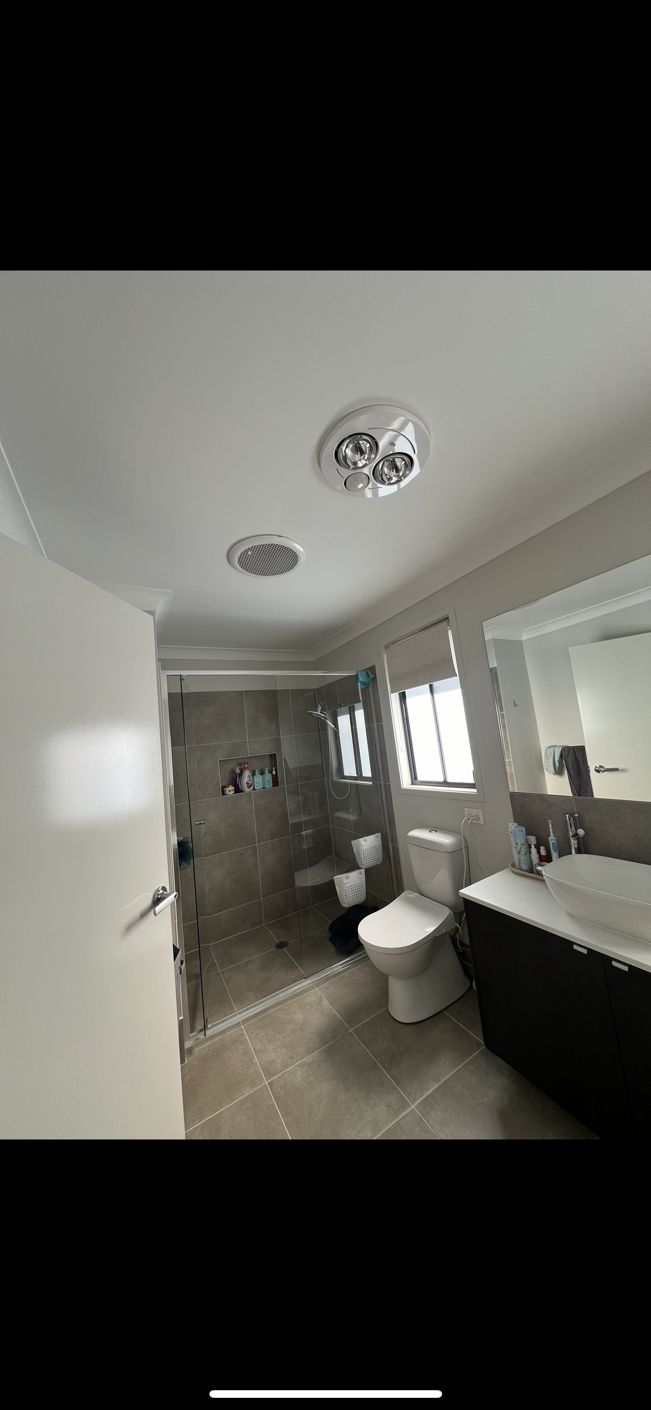 Bathroom with shower, toilet, and sink. White walls, gray tile, and two ceiling lights are visible.