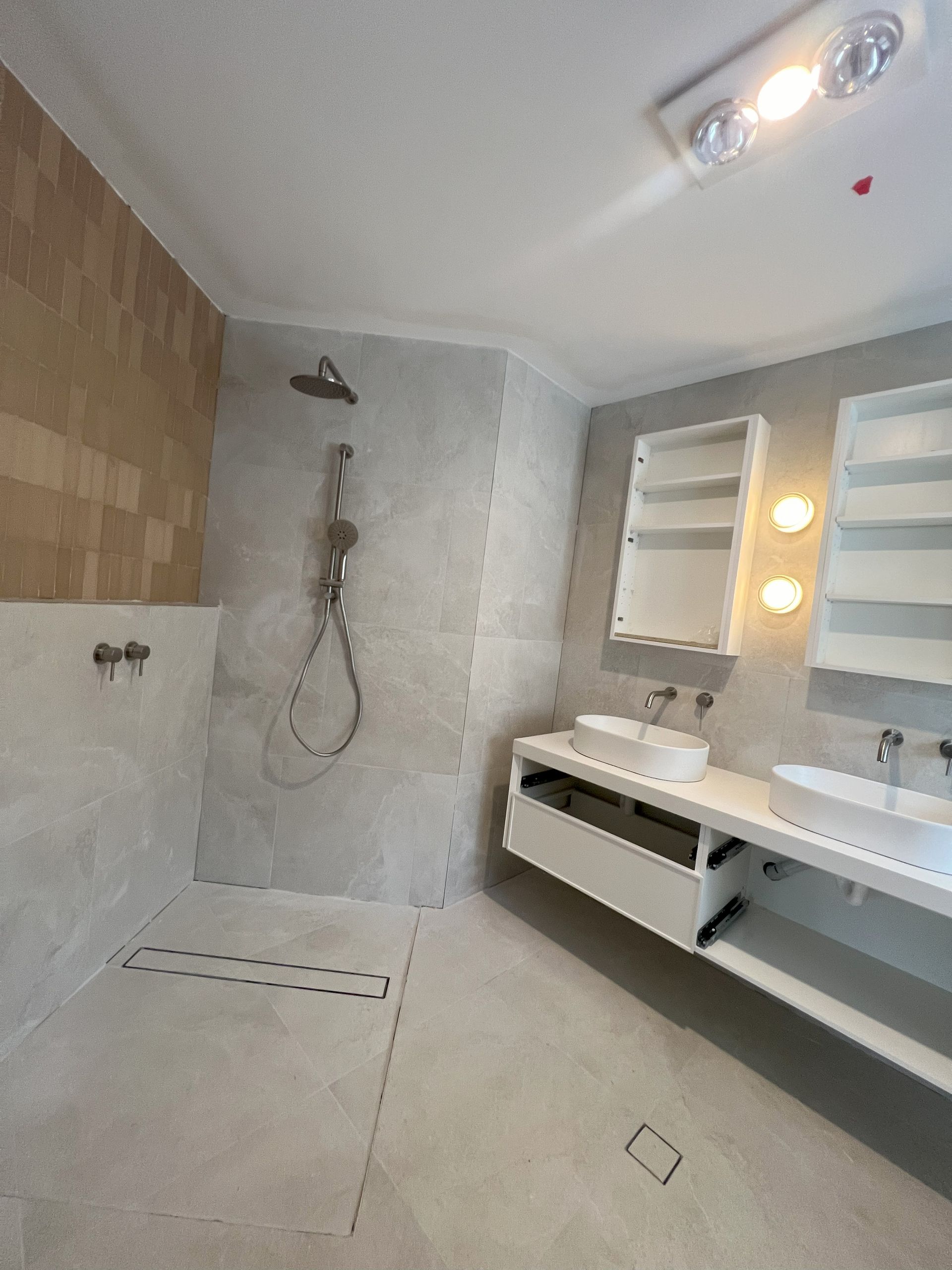 Modern bathroom with gray tile, shower, double sinks, and a cabinet with mirror.