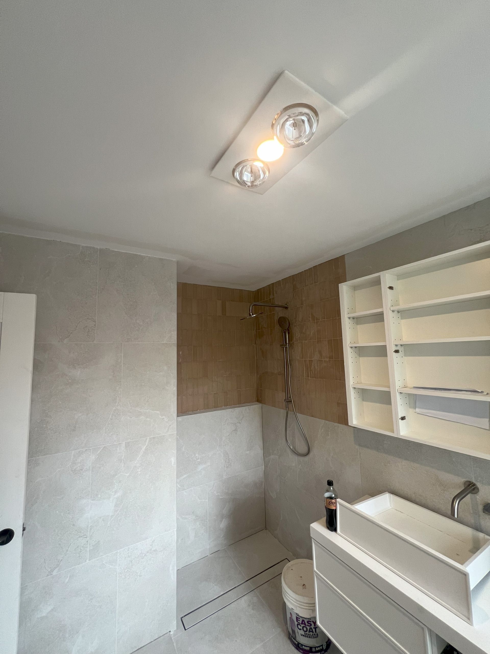 Bathroom with shower, sink, cabinet; neutral tones with textured walls, white fixtures, overhead light.