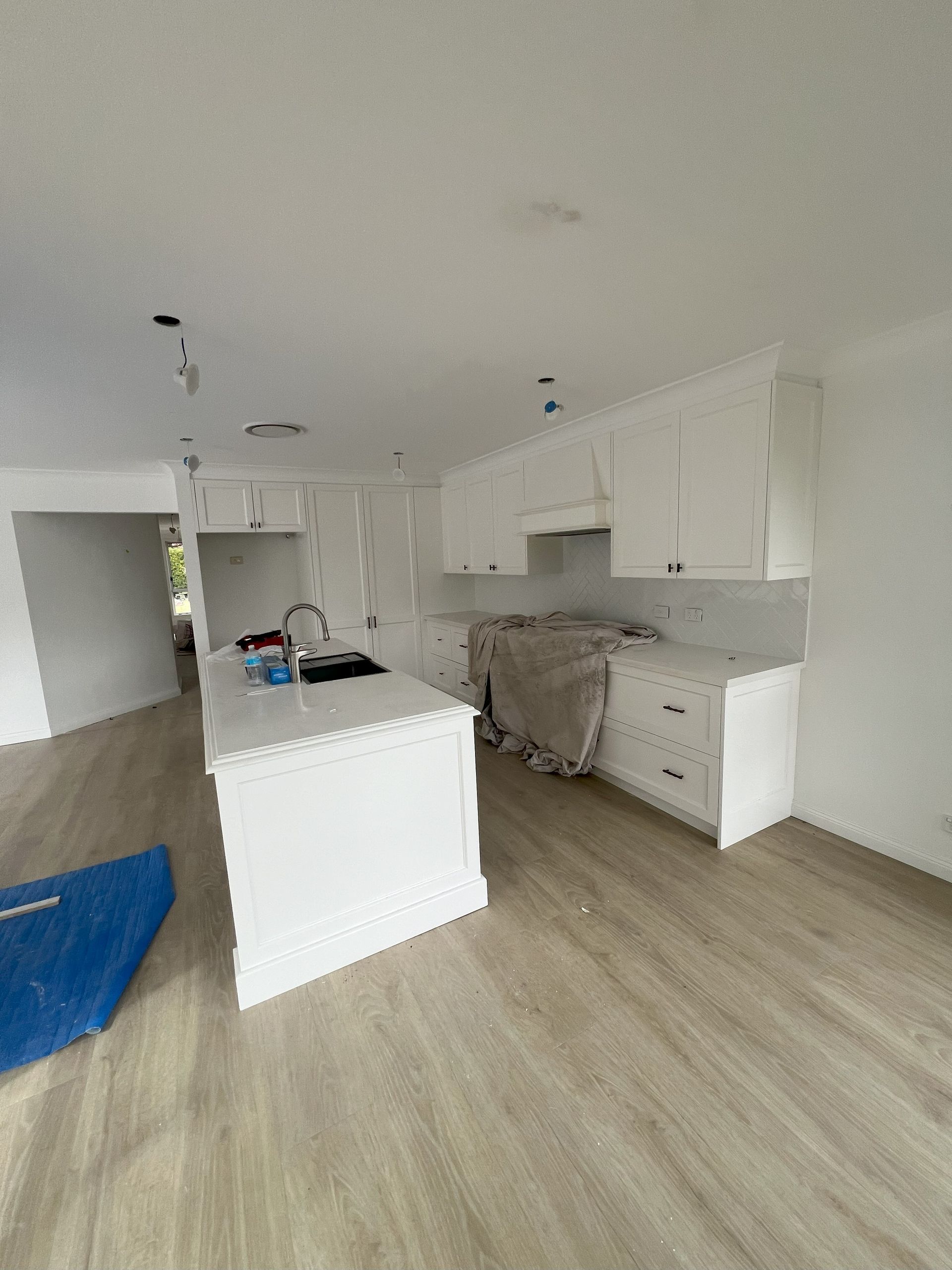 White kitchen with island and cabinets, light wood floors, marble backsplash, and unfinished drywall.